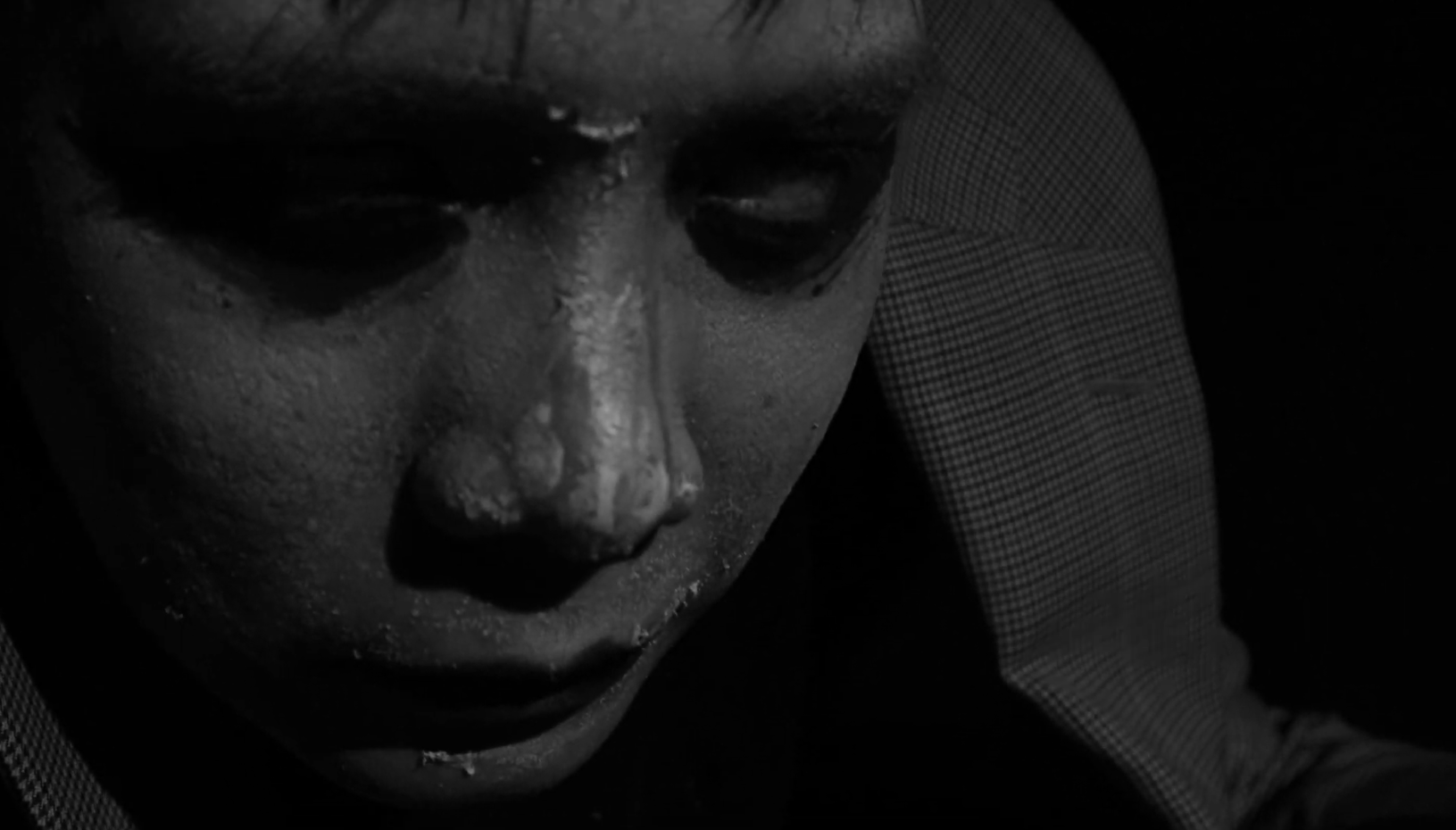 Close-up of a person's face wearing a metallic mask, with only one eye visible, in a dark setting.