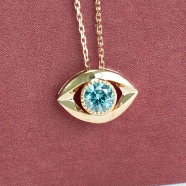 A striking memorial necklace with a big blue diamond set in a unique gold eye-shaped pendant, displayed on a mauve background.
