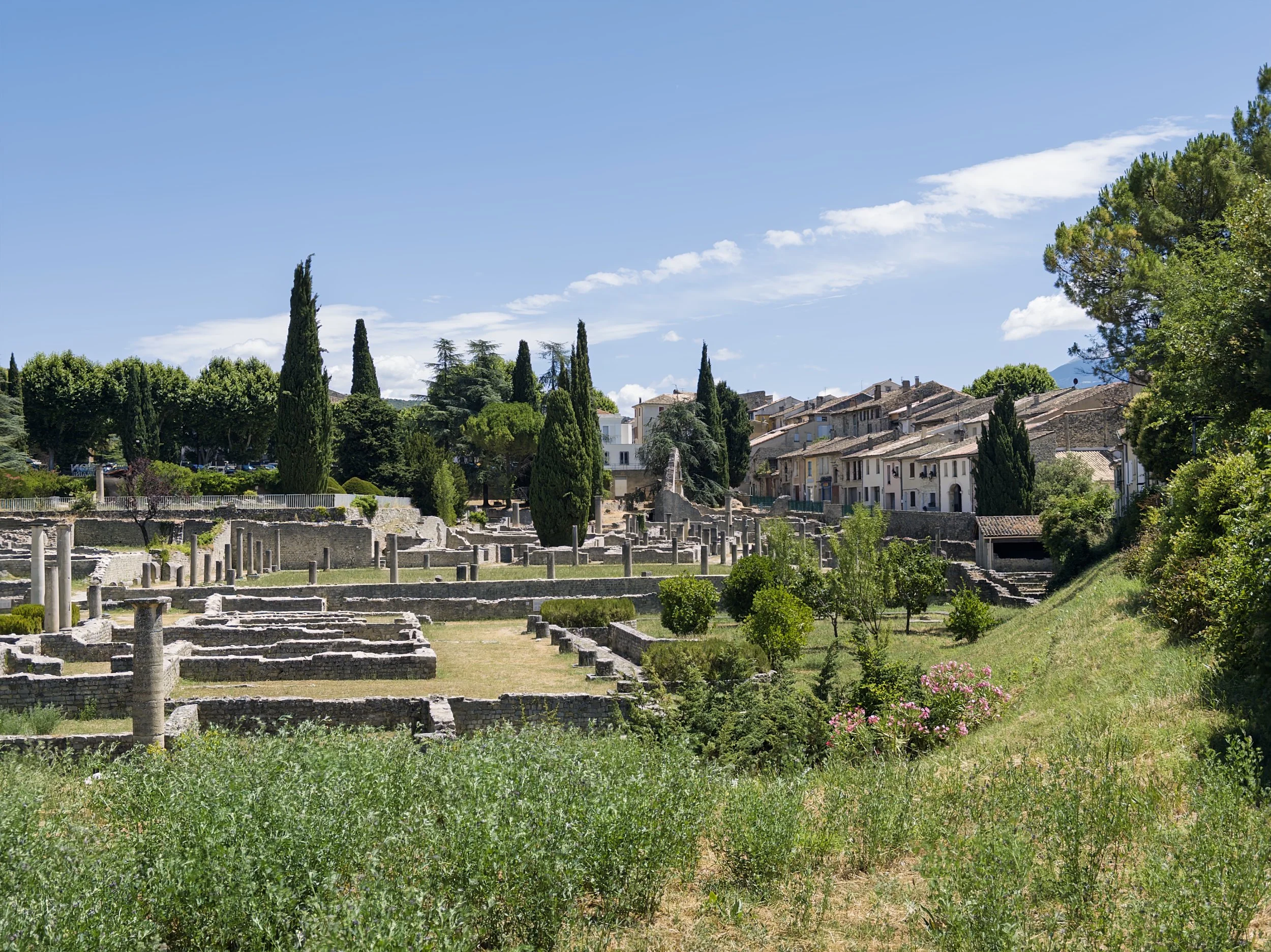 Ruines antiques avec colonnes et végétation verdoyante sous un ciel bleu clair dans une ville en Italie.