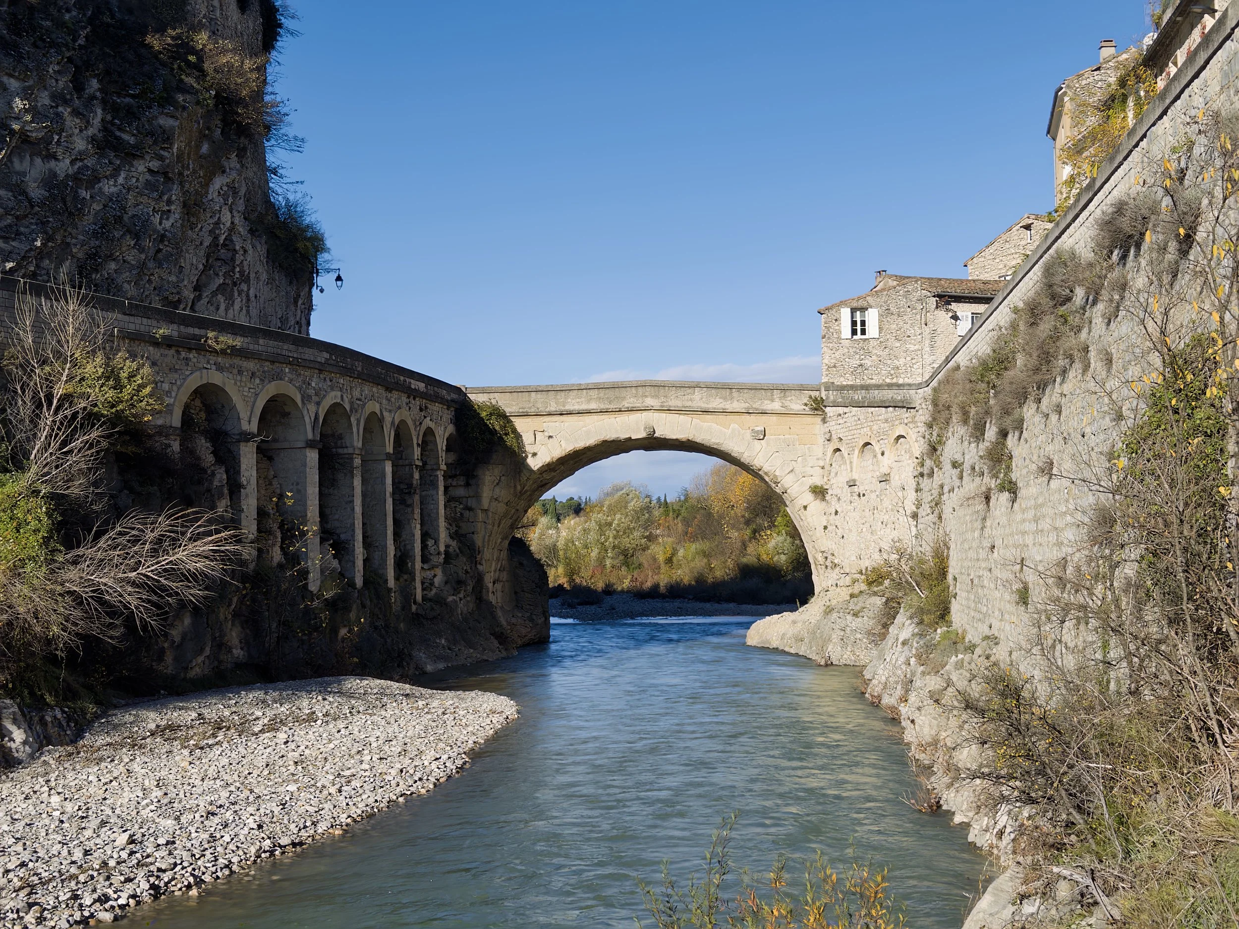 Pont en pierre au-dessus d'une rivière, entouré de bâtiments en pierre et de végétation.