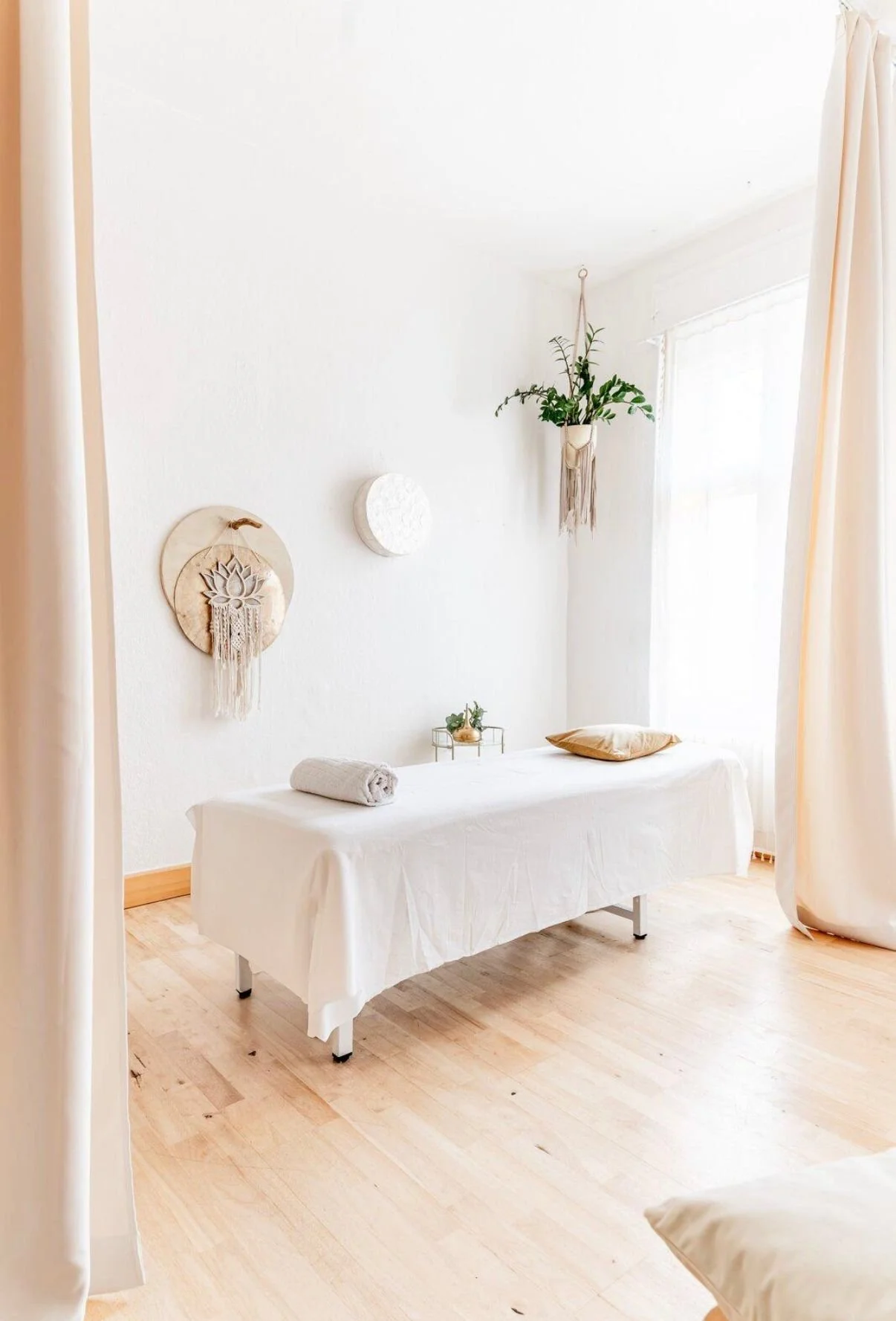 Behandlungsraum mit Massagebett, weißen Wänden, Pflanzen und natürlichem Licht