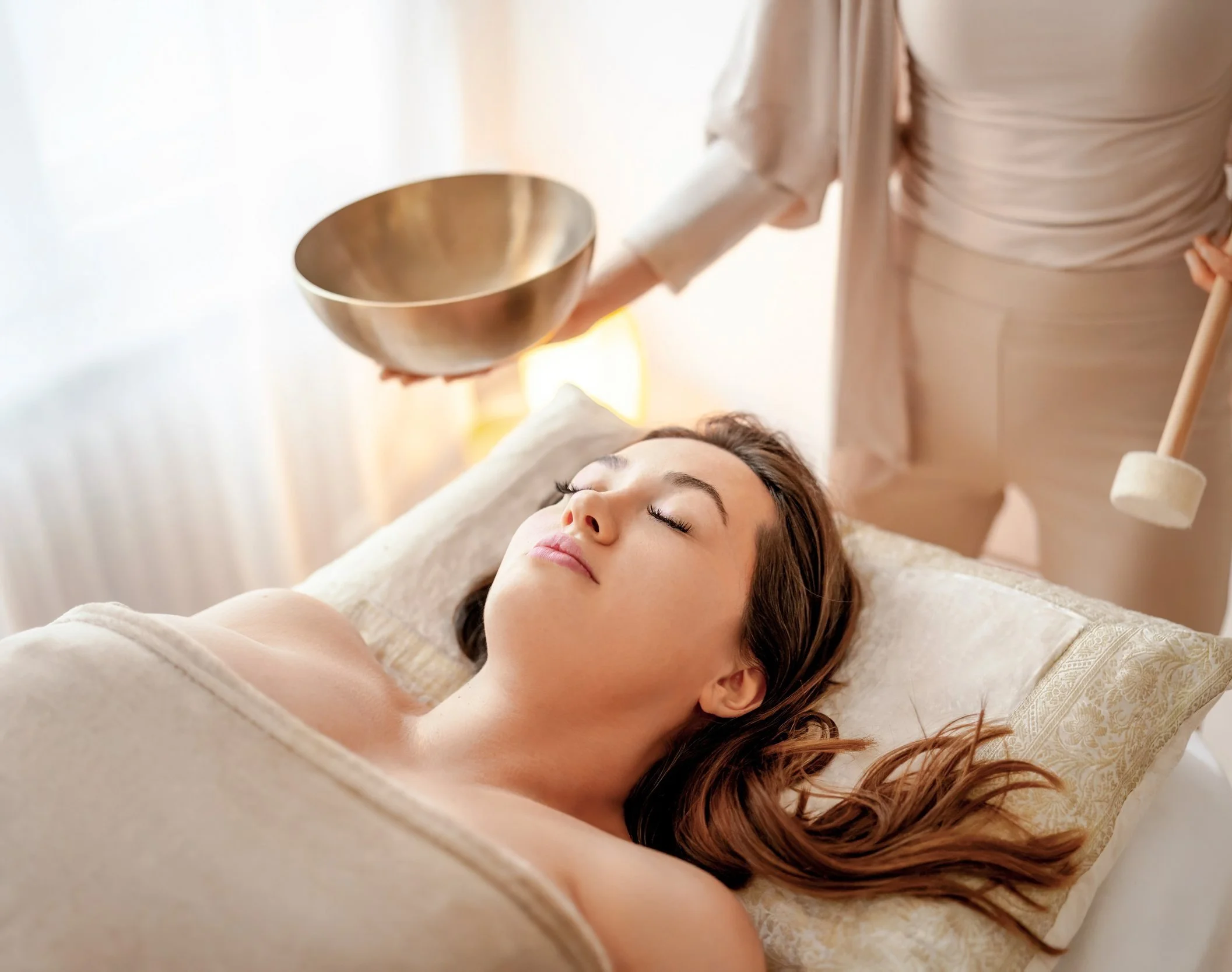 Frau erhält eine Klangschalentherapie im Spa, während sie entspannt auf einem Liege liegt.