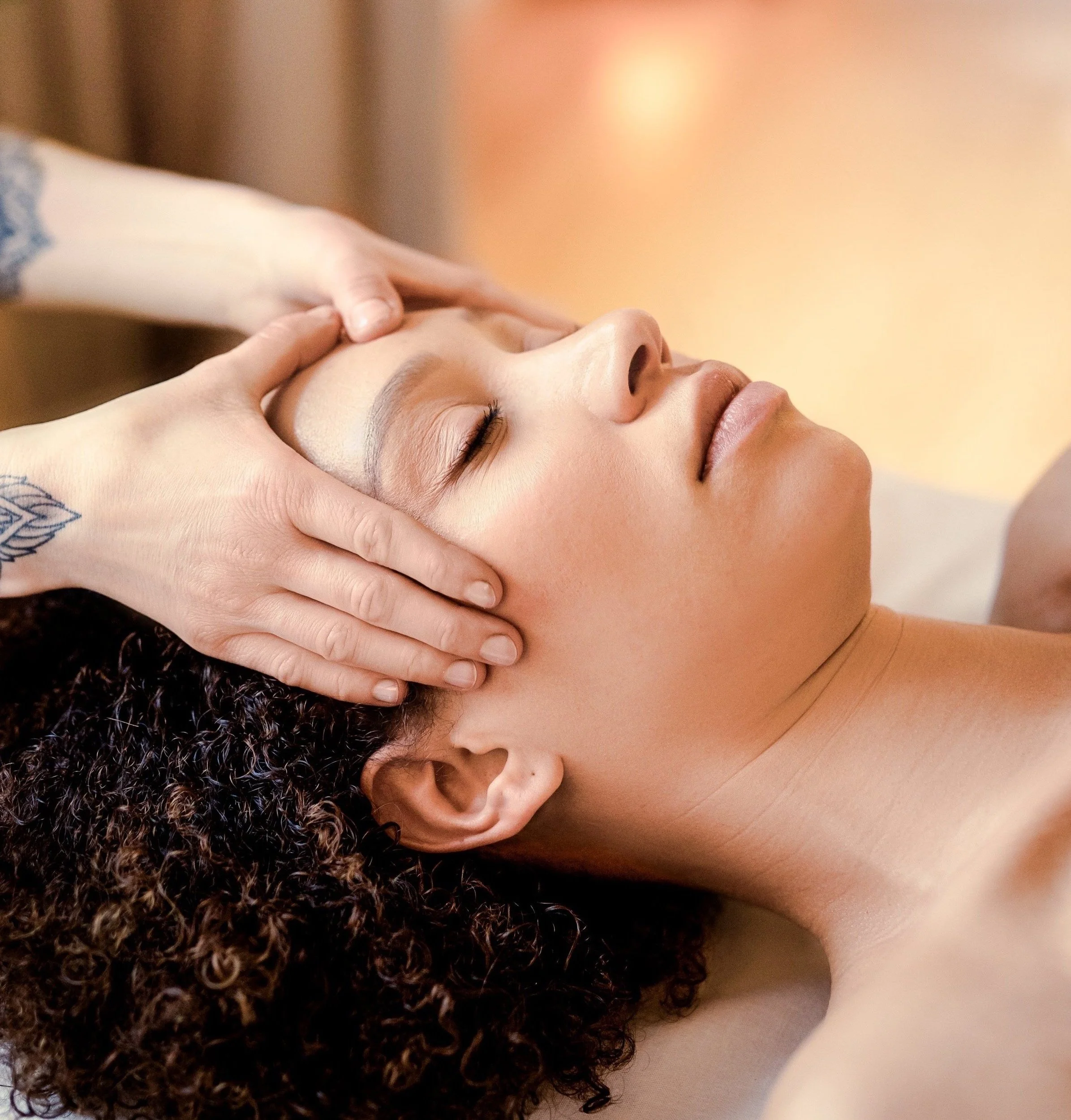 Frau erhält eine Massage am Kopf in einem Spa. Große Handflächen massieren die Stirn und den Kopf der Frau, während sie entspannt liegt.