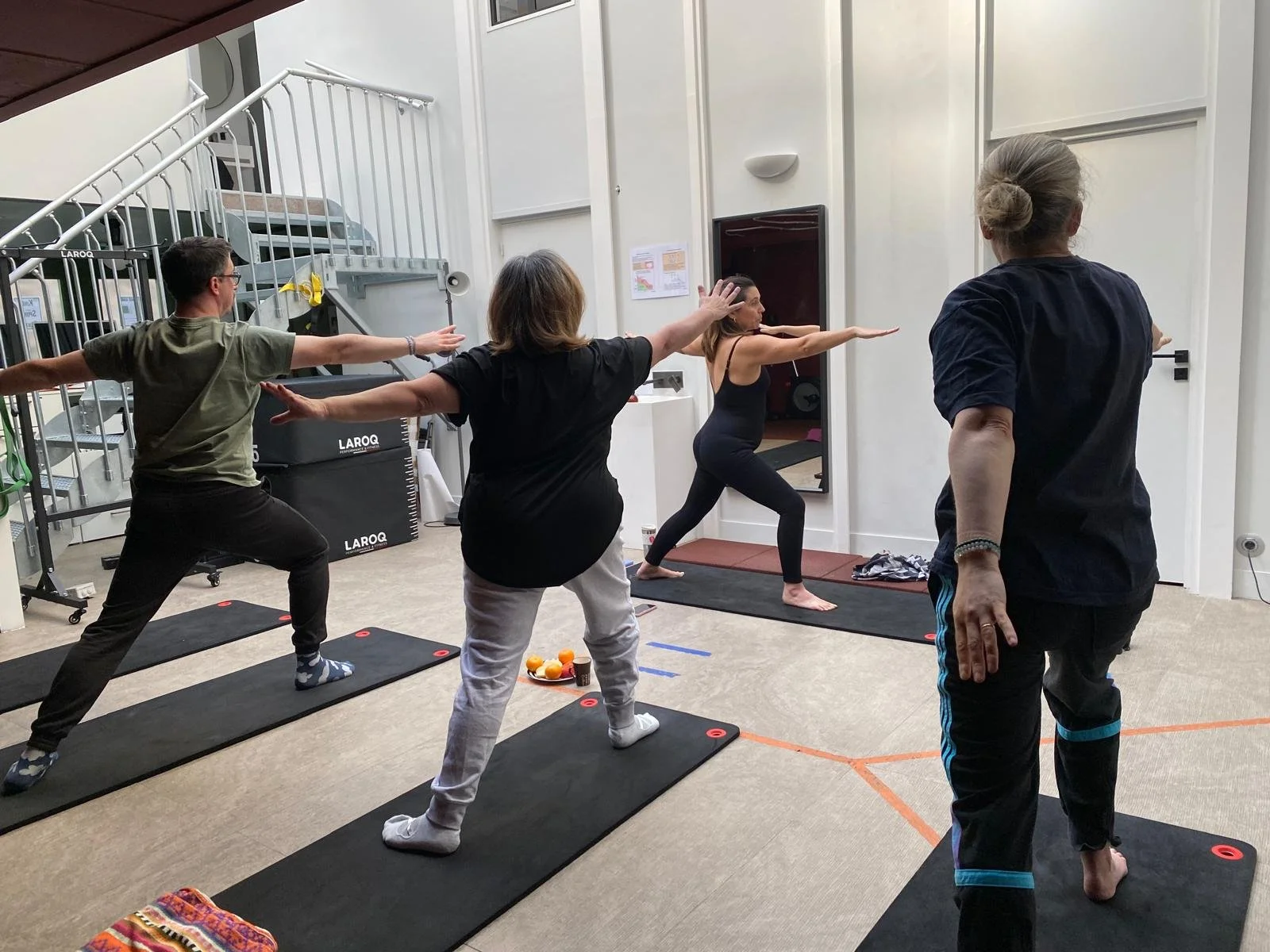 Groupe de personnes en train de faire une séance de yoga dans une salle, avec une femme en position de squat et d'autres personnes en position de bras étendus.