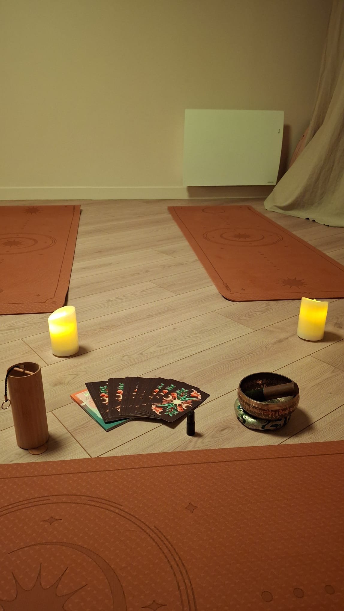 Indoor space with yoga mats, tarot cards, candles, and singing bowl arranged on the floor, suggesting a meditation or spiritual practice setting.