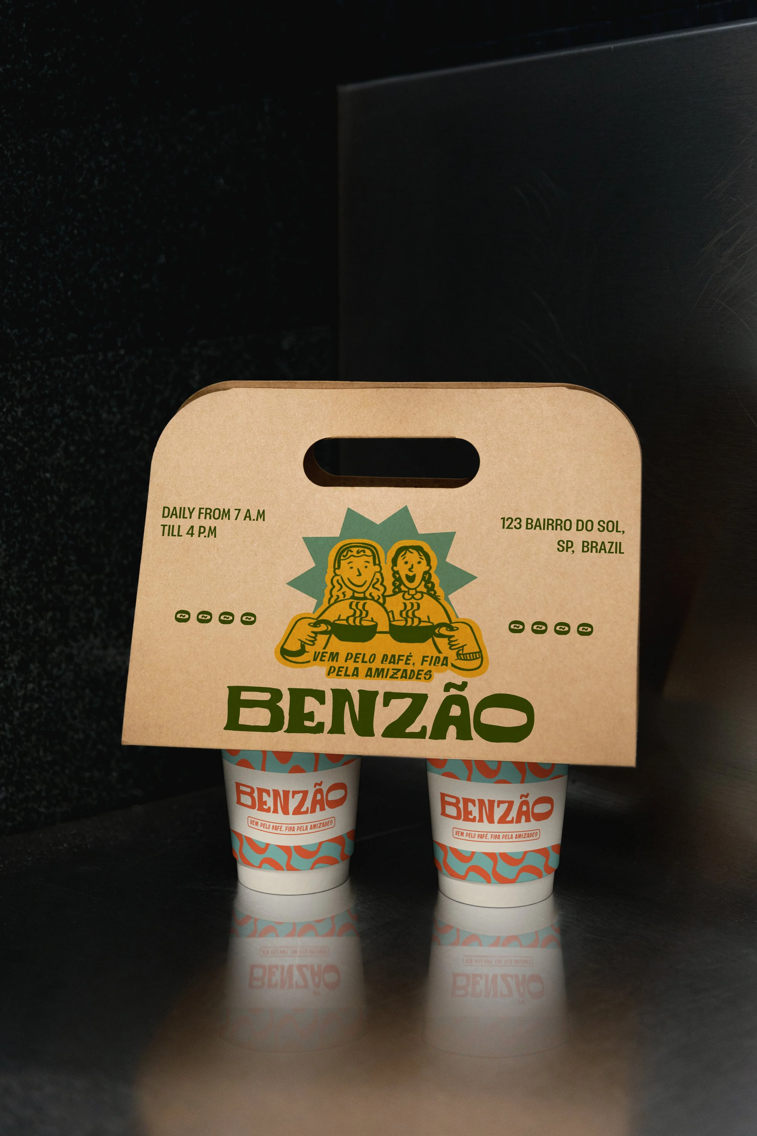 Two cups of coffee with a cardboard carrying tray on top, featuring a logo with two women holding coffee cups and text in Portuguese, next to a black background.