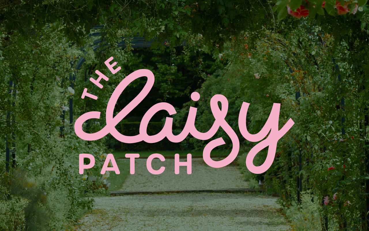 A garden pathway surrounded by greenery and flowers with a sign that says 'The Lazy Patch' in pink cursive text.
