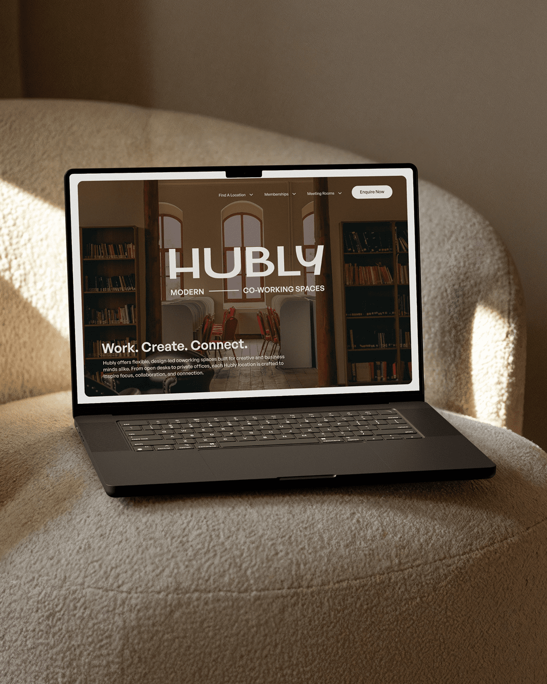 Laptop on a beige armchair displaying a website for Hubly, a modern co-working space with a focus on work, creativity, and connection.