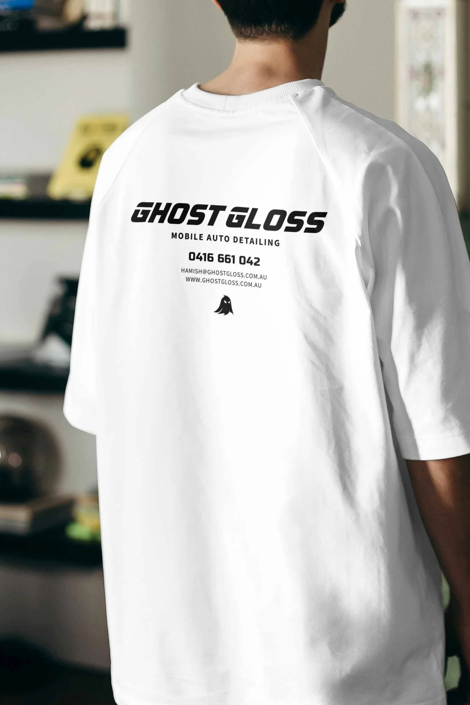 Person wearing a white t-shirt with black text and a small ghost logo on the back, promoting Ghost Gloss Mobile Auto Detailing.