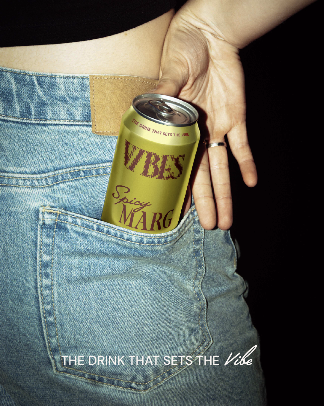 Close-up of a person's back pocket with a yellow can of WYES spicy margarita drink partially inside. The person is wearing light blue jeans and a black top. The text overlay reads "THE DRINK THAT SETS THE Vibe" and "THE VIBE".