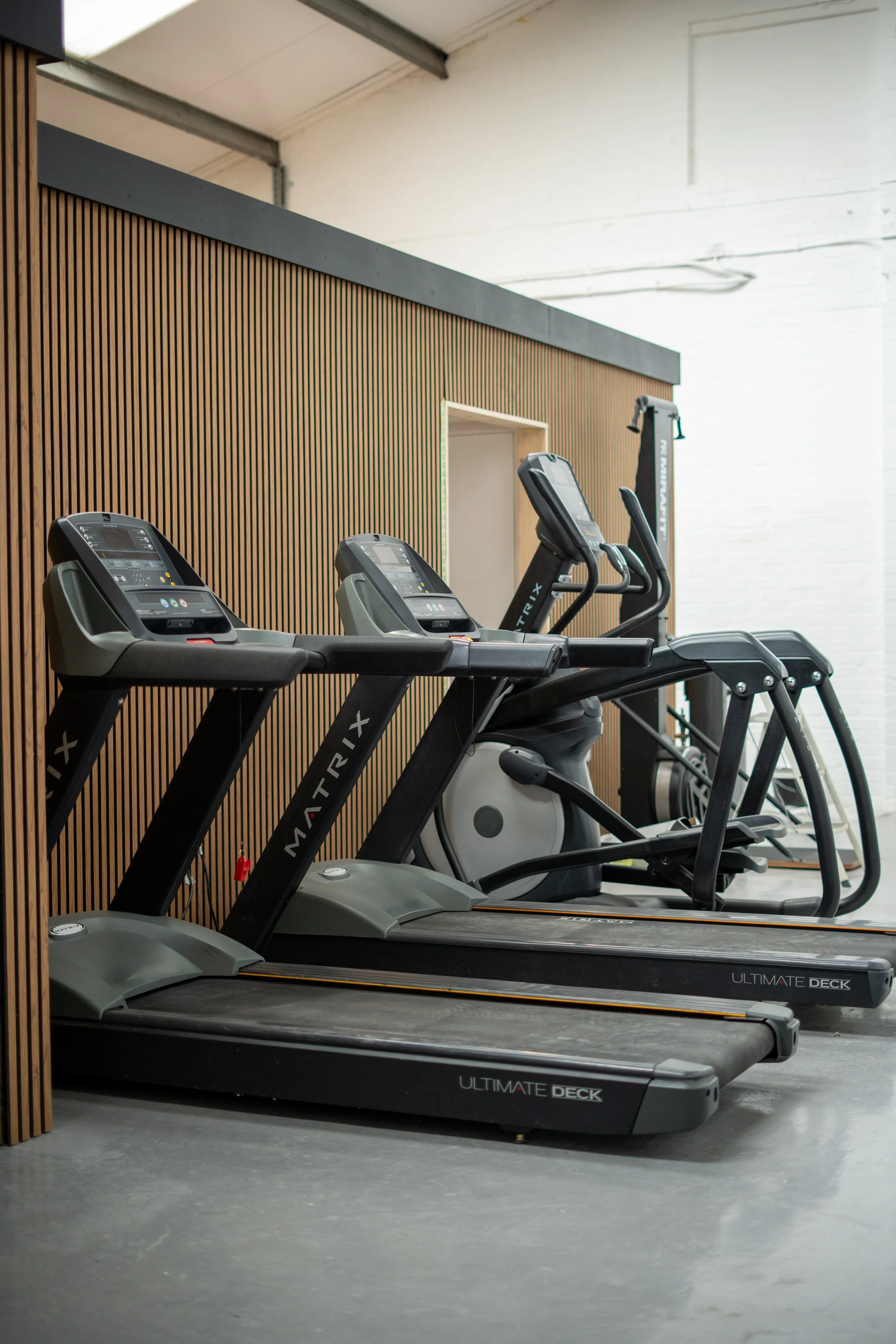 Three treadmills in a gym with wooden and white wall background.