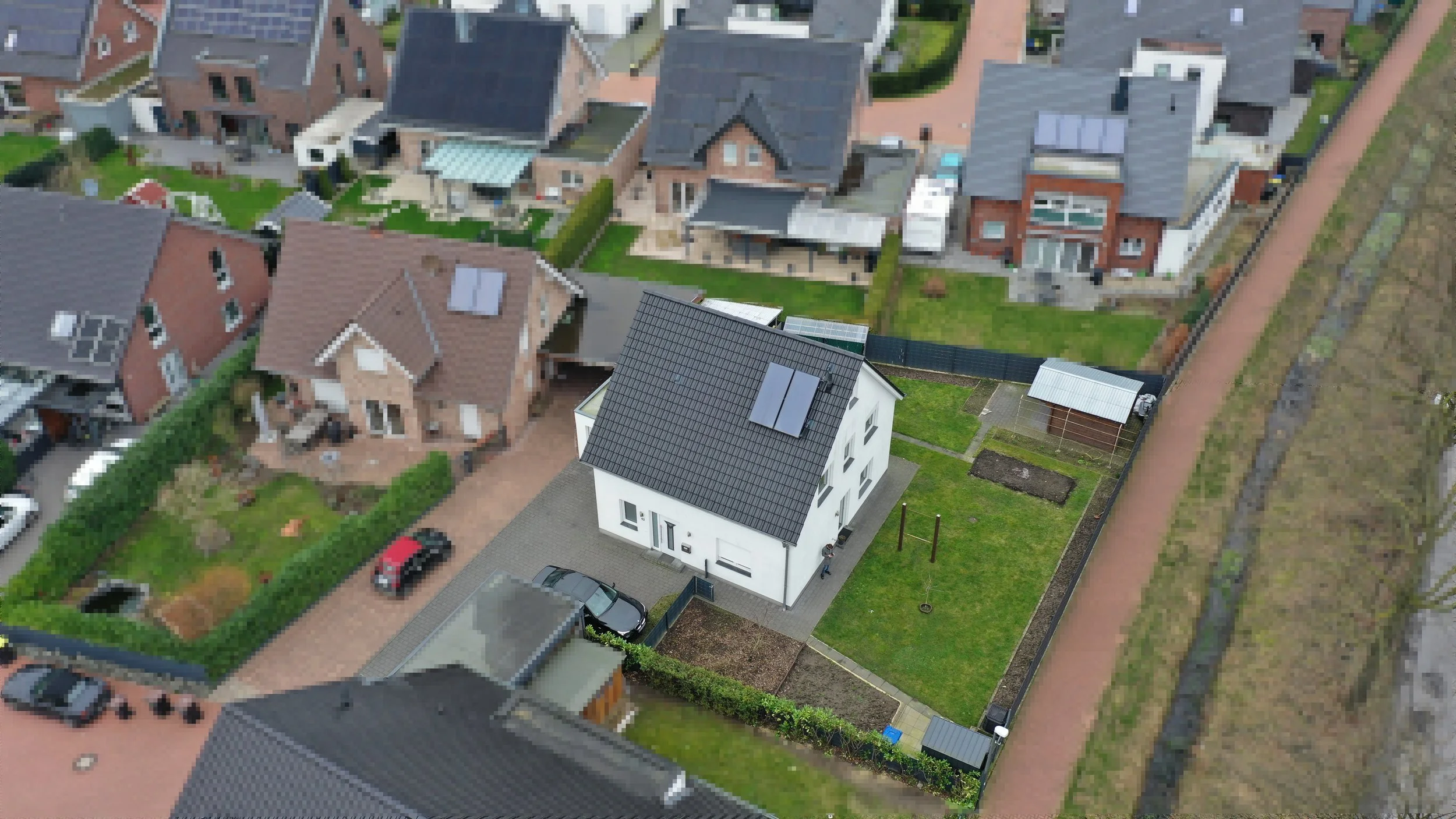 Luftaufnahme eines Hauses mit solarbetriebener Dachfläche, umgeben von einem Garten und Nachbarhäusern in einer Wohnsiedlung.