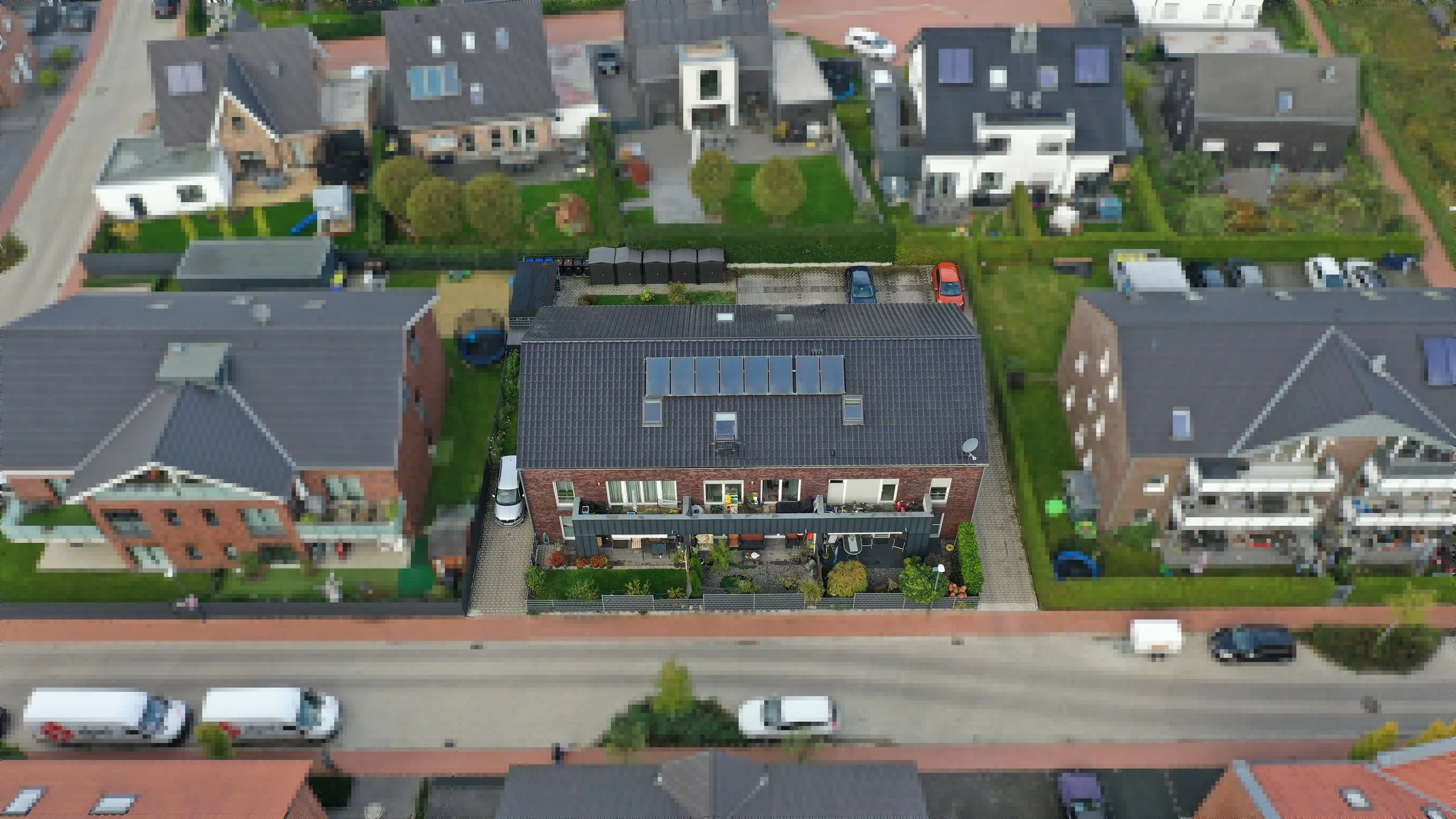 Luftaufnahme eines Mehrfamilienhauses mit Garten, Parkplätzen und umliegenden Wohnhäusern in einer Wohnsiedlung.