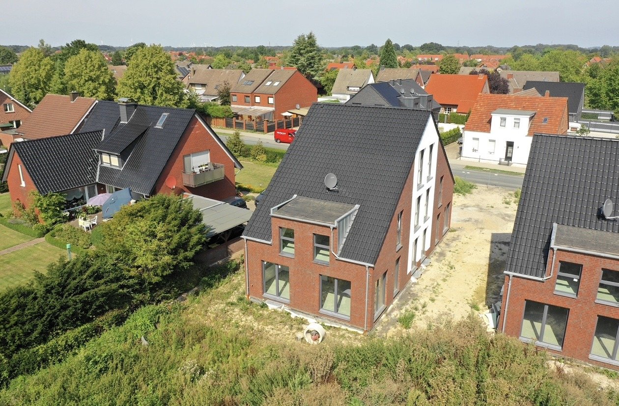 Ein Neubau in einem Wohngebiet mit modernen roten Backsteinhäusern und schwarzen Dächern, teilweise noch im Bau befindlich, umgeben von Grünflächen.