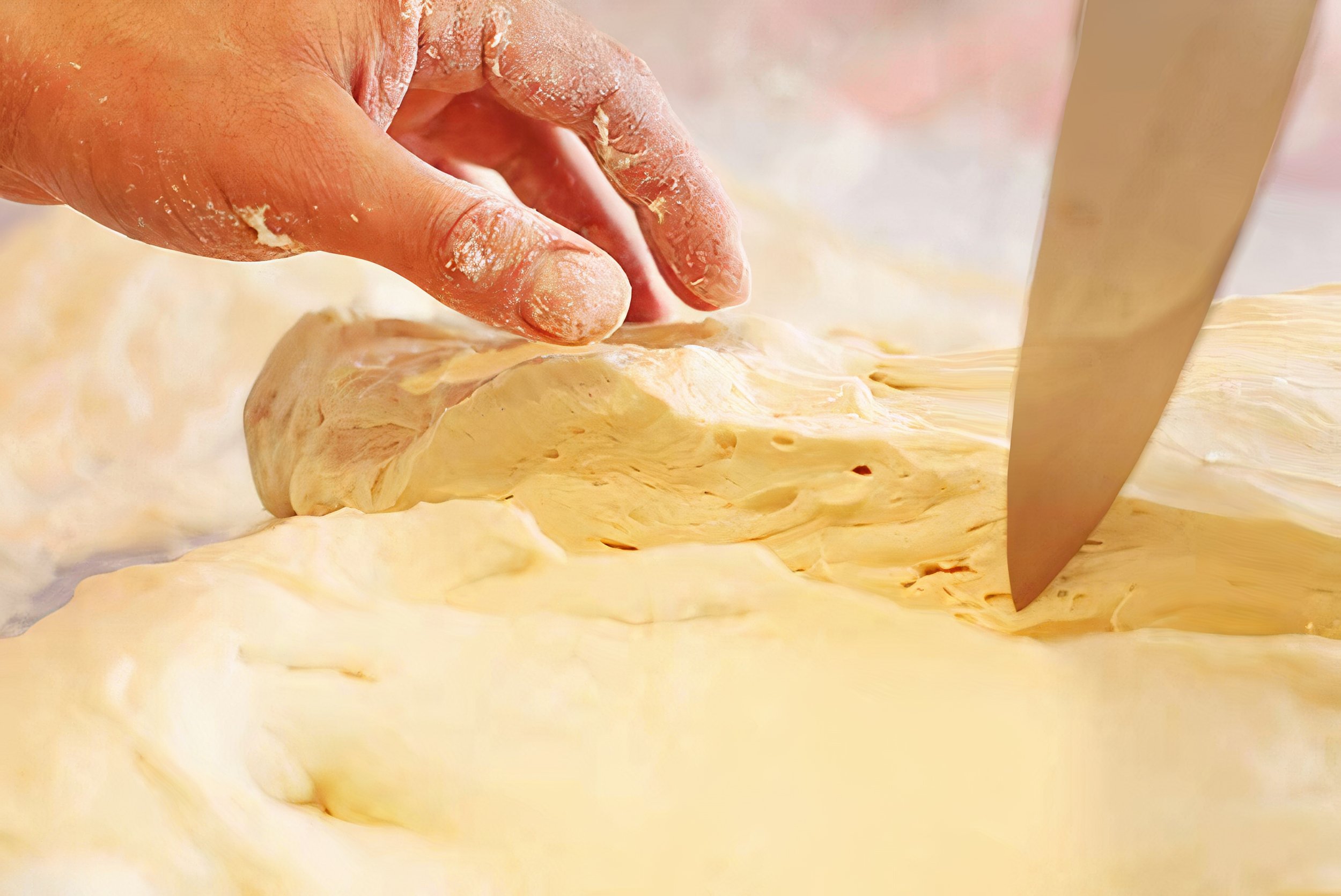 Hand cutting a dough with a knife, seasoned with flour