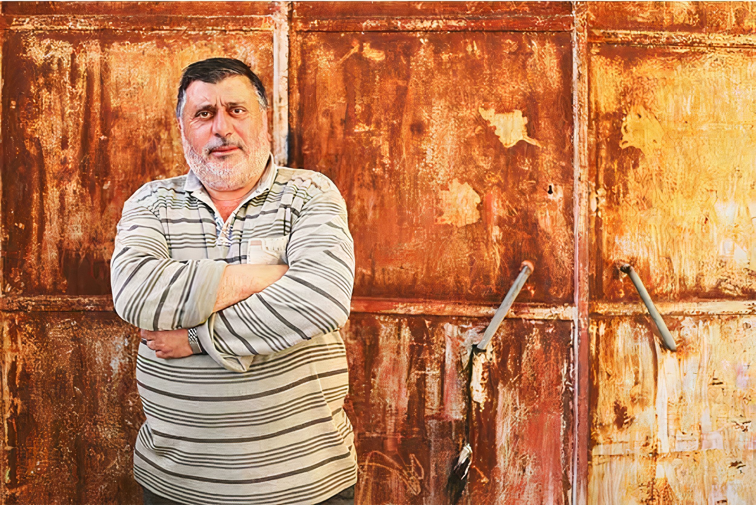 Elderly man with beard and striped shirt in front of rusty metal panels
