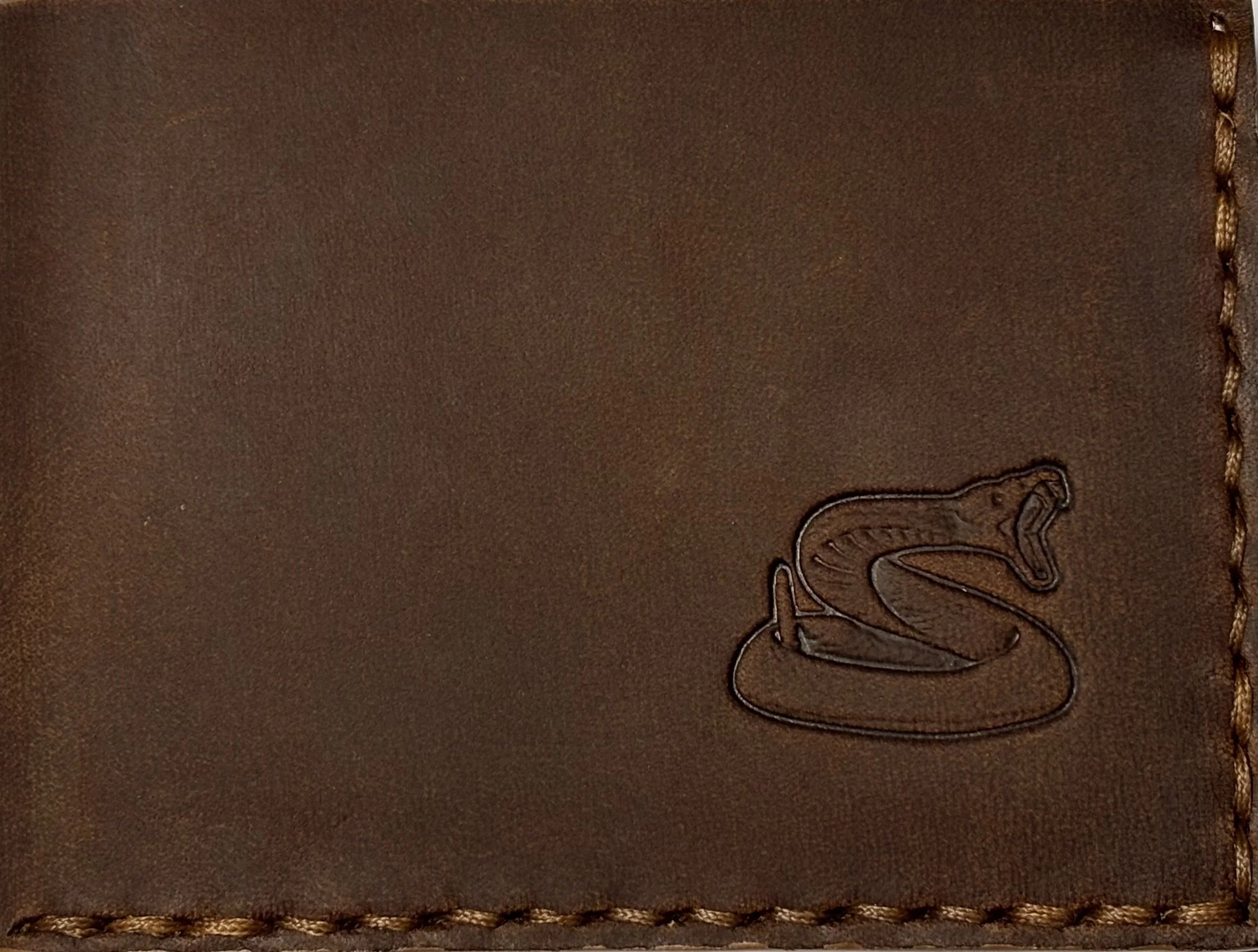 Macro view of brown leather displaying fine hand saddle stitching and a stamped rattlesnake logo.