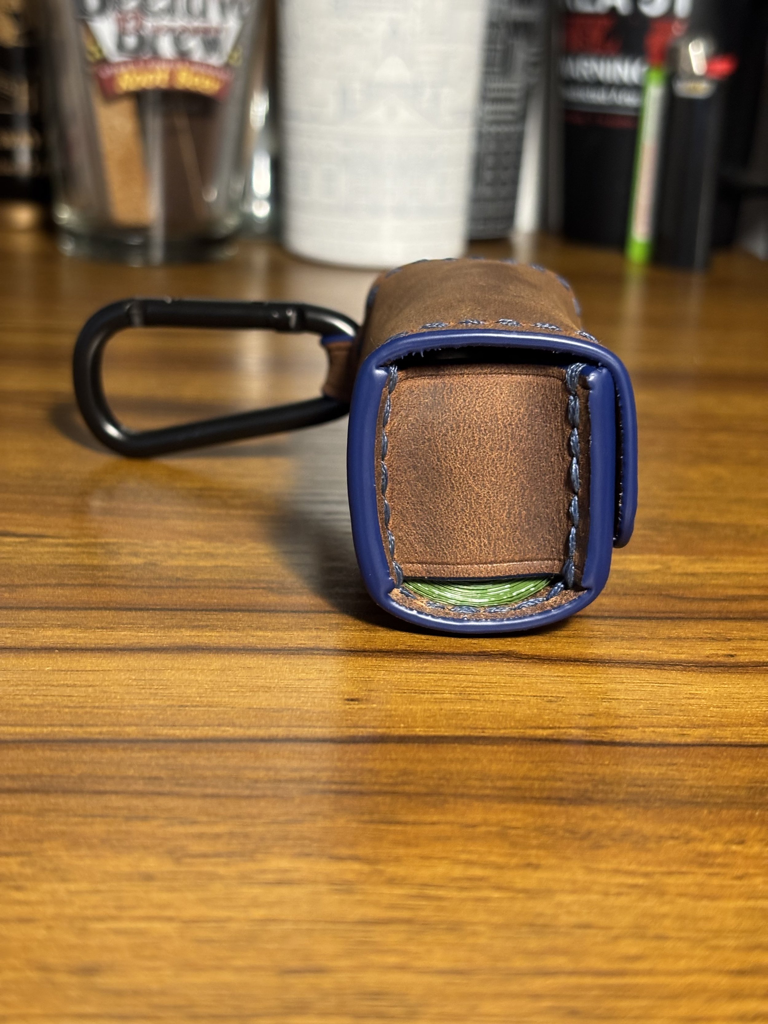 Side profile of leather dog waste bag dispenser showing dispenser opening and carabiner clip.