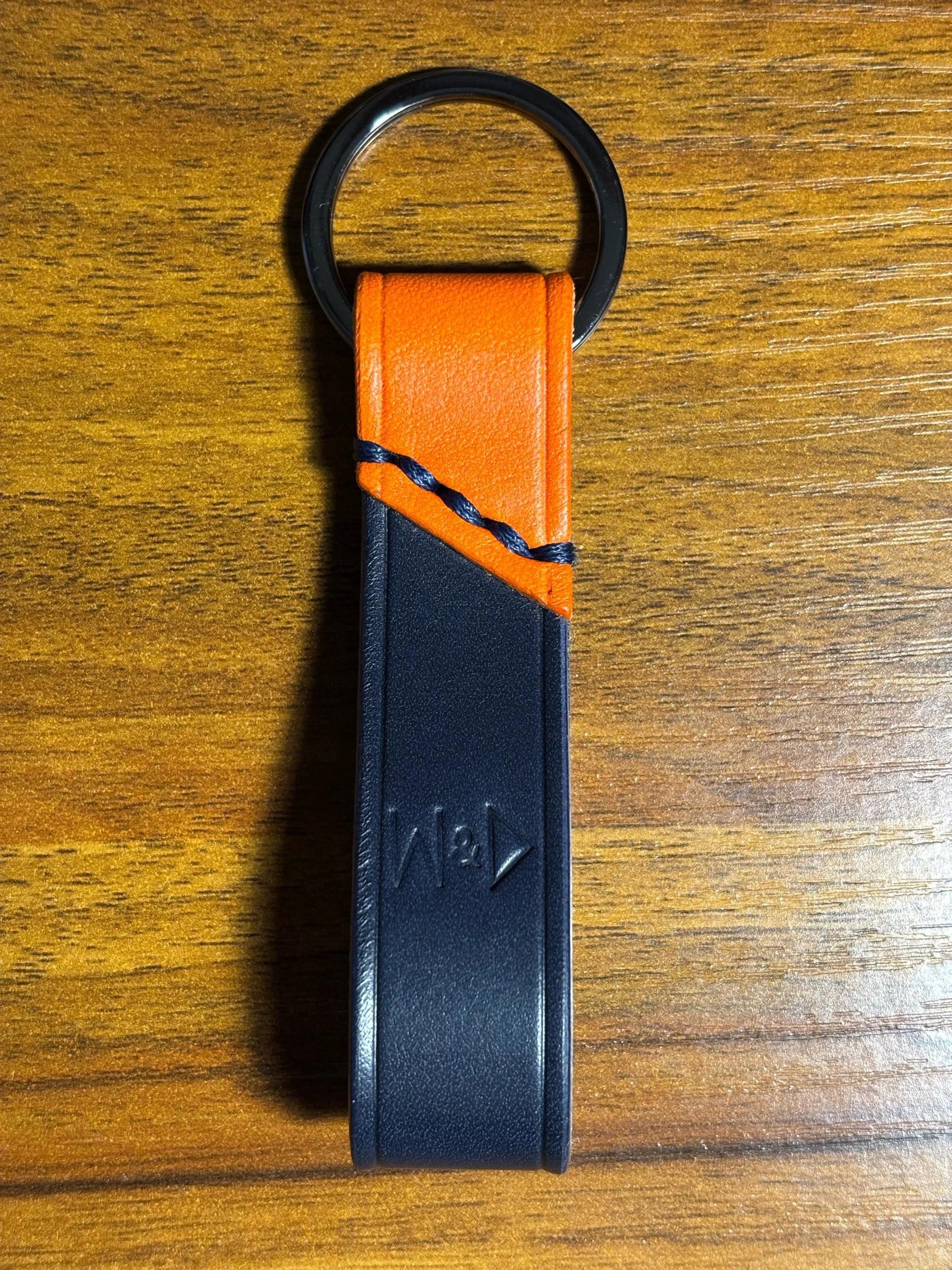 Handcrafted black and orange leather key holder fob with blue contrast stitching and stamped maker's mark logo.