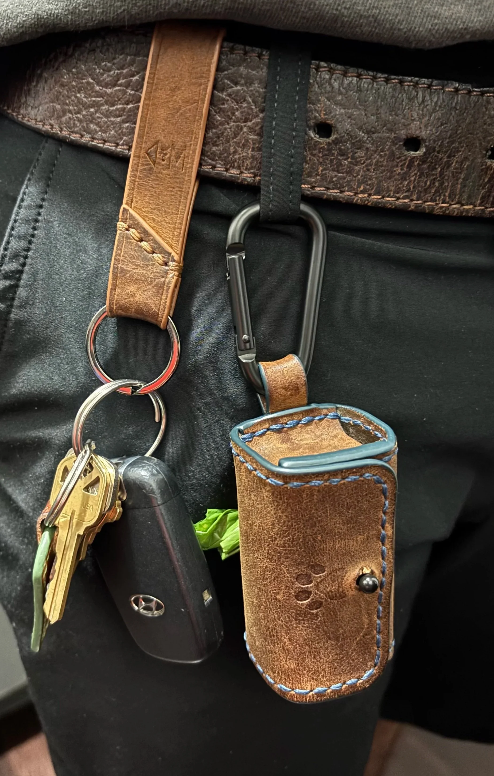 Handcrafted leather dog waste bag dispenser and key fob clipped to a belt loop for everyday carry.