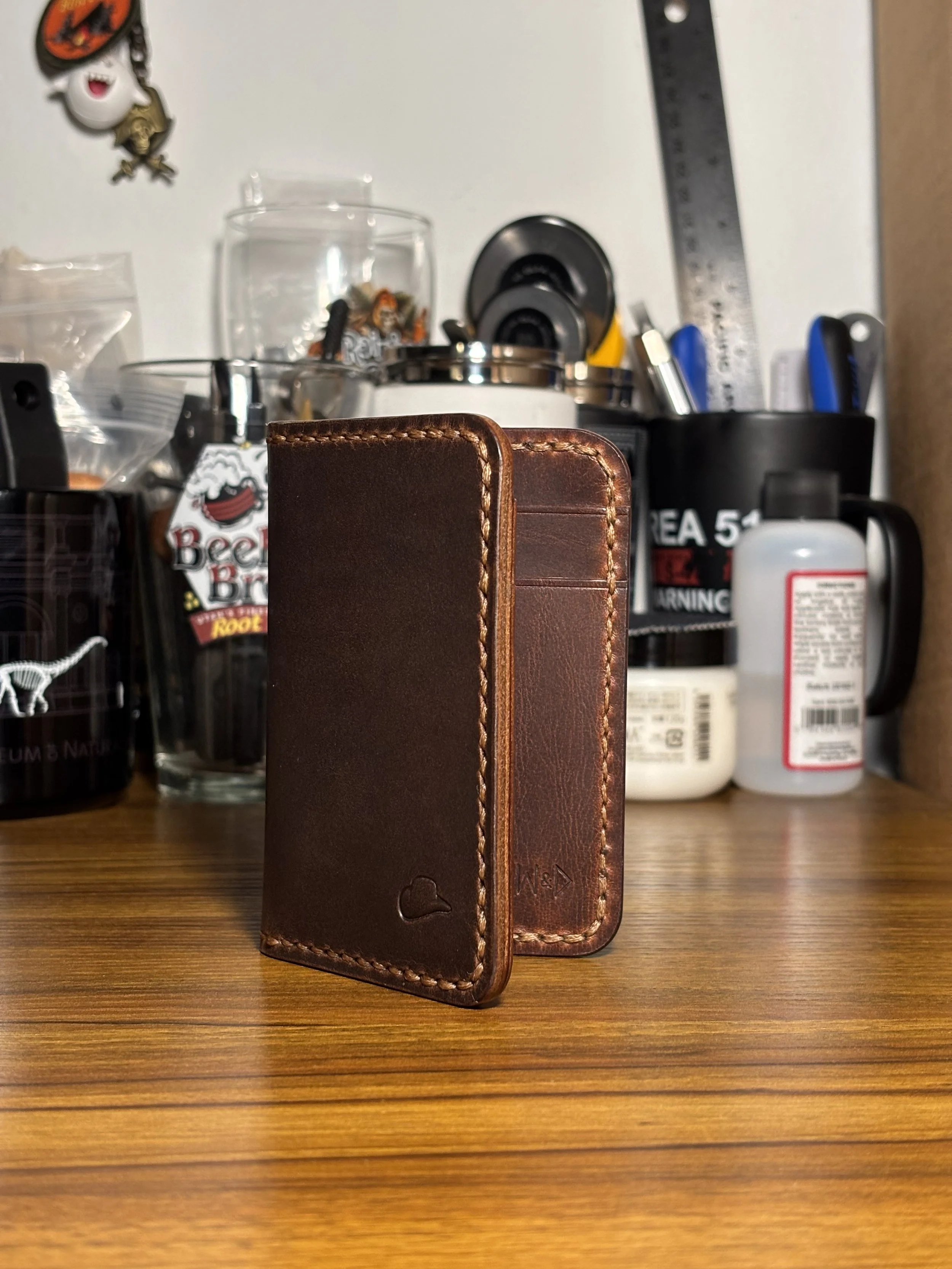 The cowboy handmade brown leather bifold wallet standing on a leatherworking bench