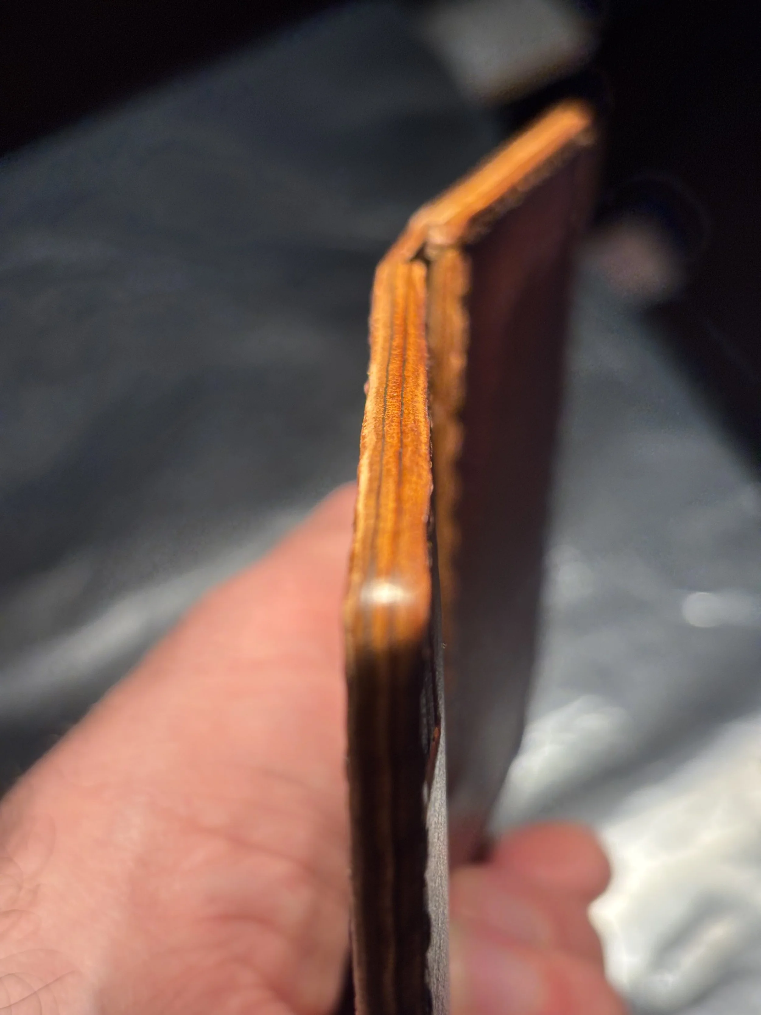 Handheld macro view highlighting traditional hand-glassed burnished edges on a brown leather wallet.