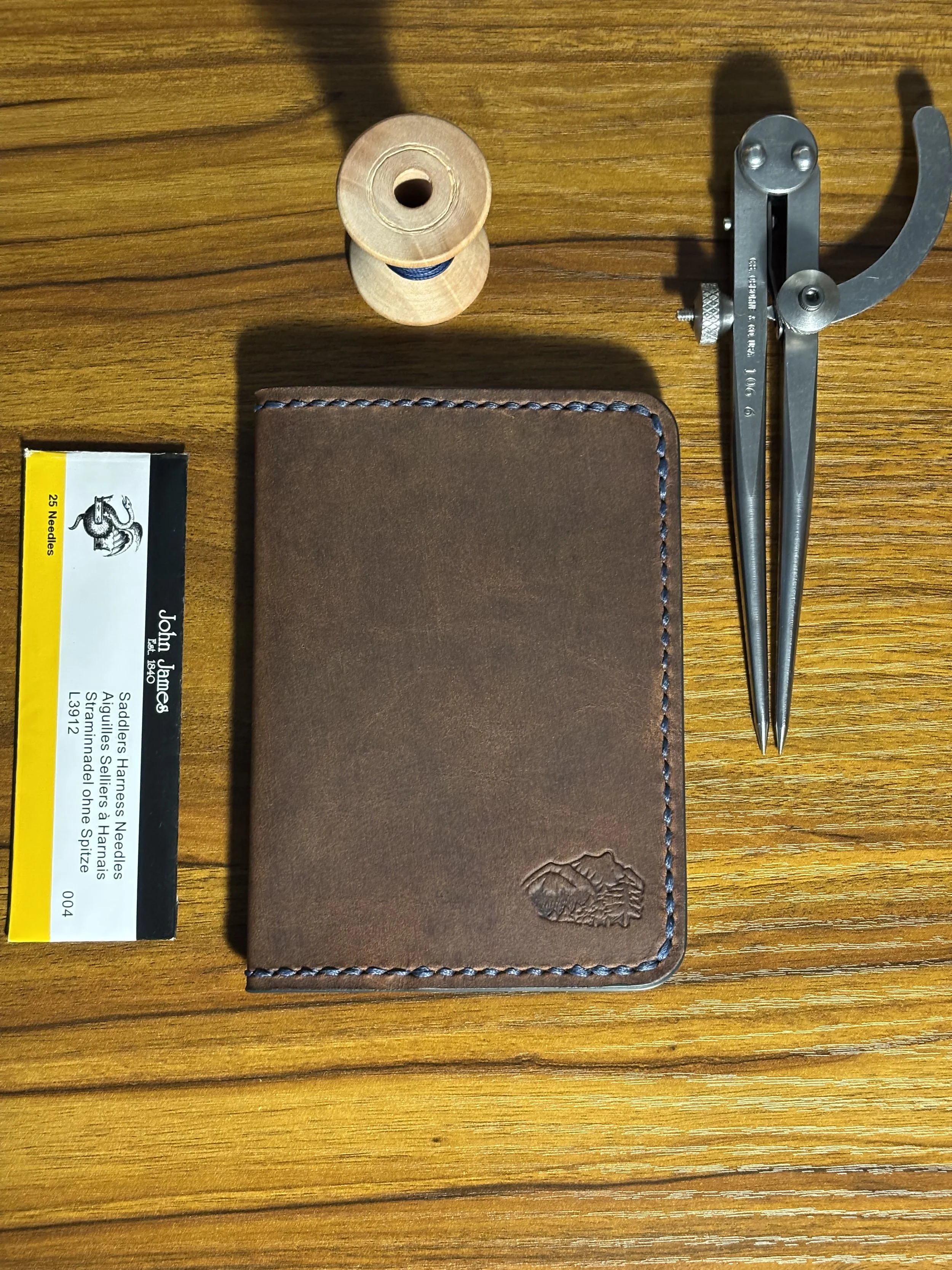 Brown leather passport case resting on a wooden workbench next to leather working tools..