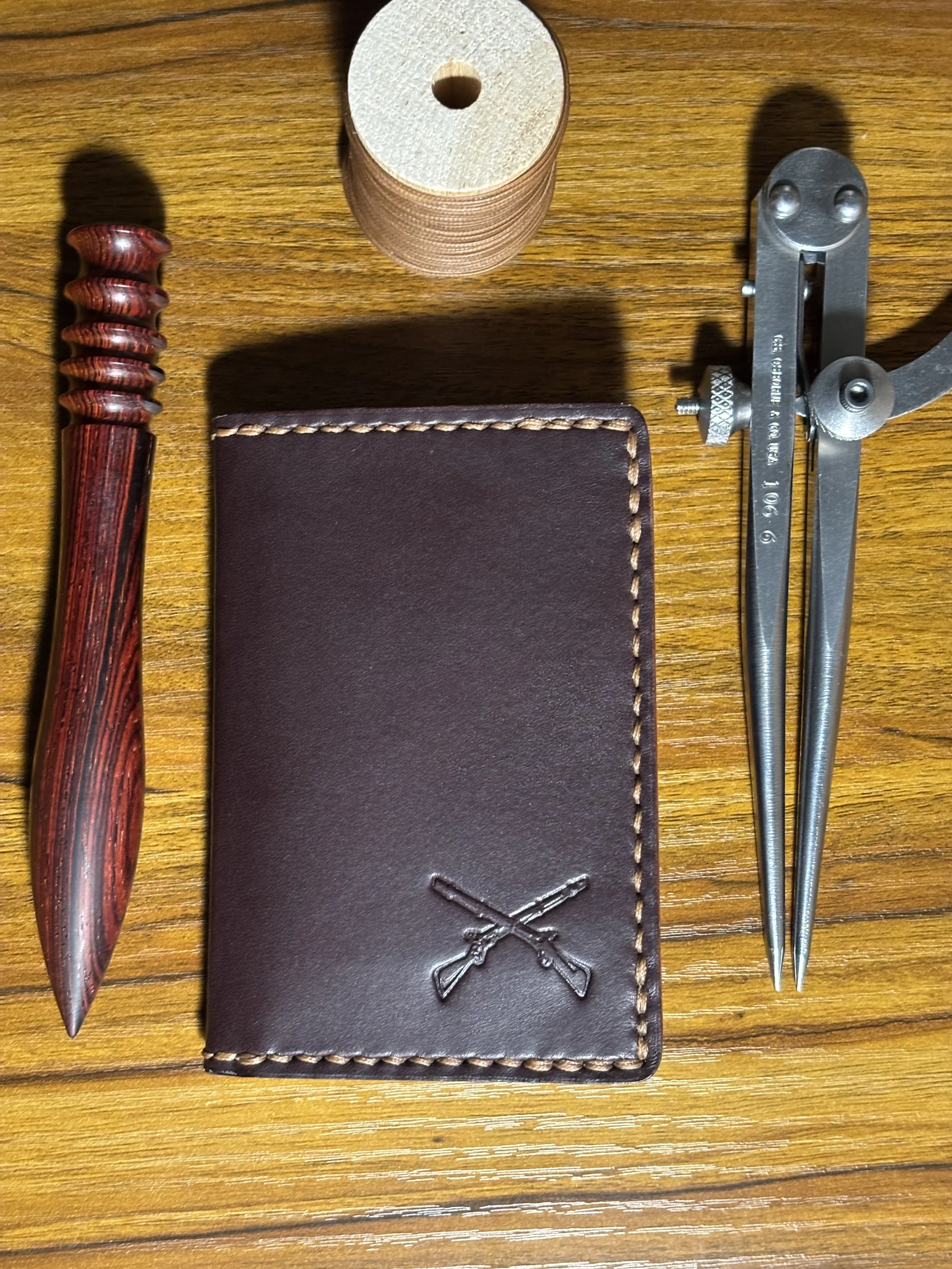 Dark brown leather bifold wallet featuring hand saddle stitching and stamped crossed rifles logo.