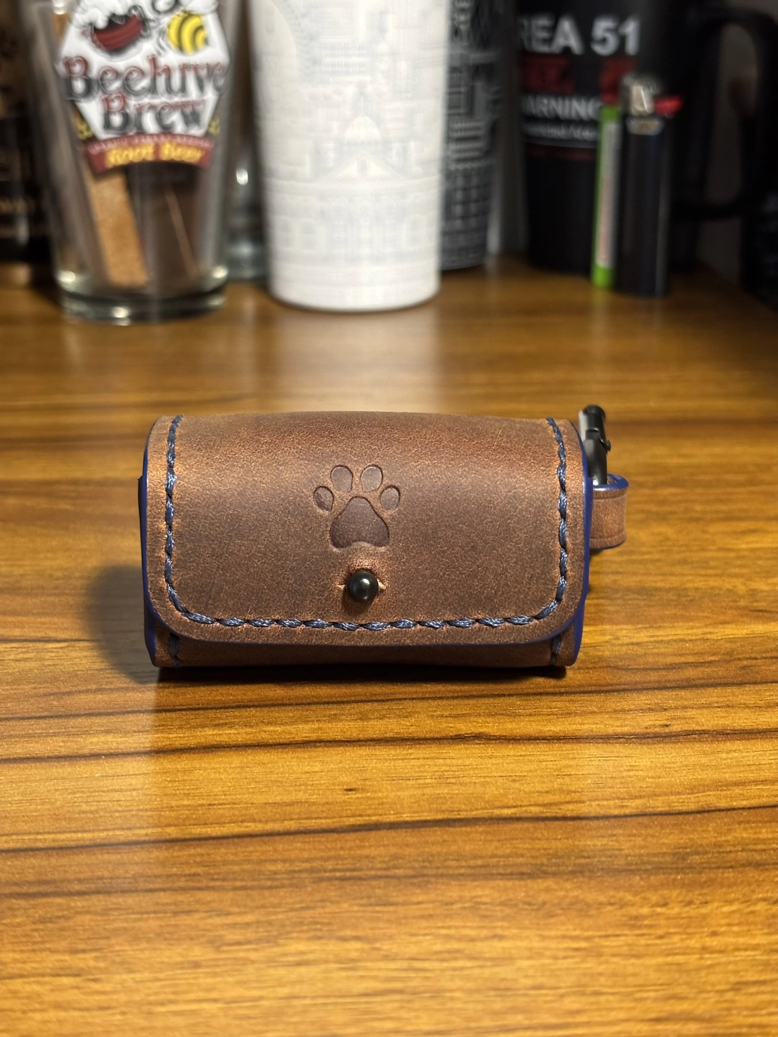 Handcrafted brown leather dog waste bag dispenser featuring a stamped paw print and blue contrasting thread