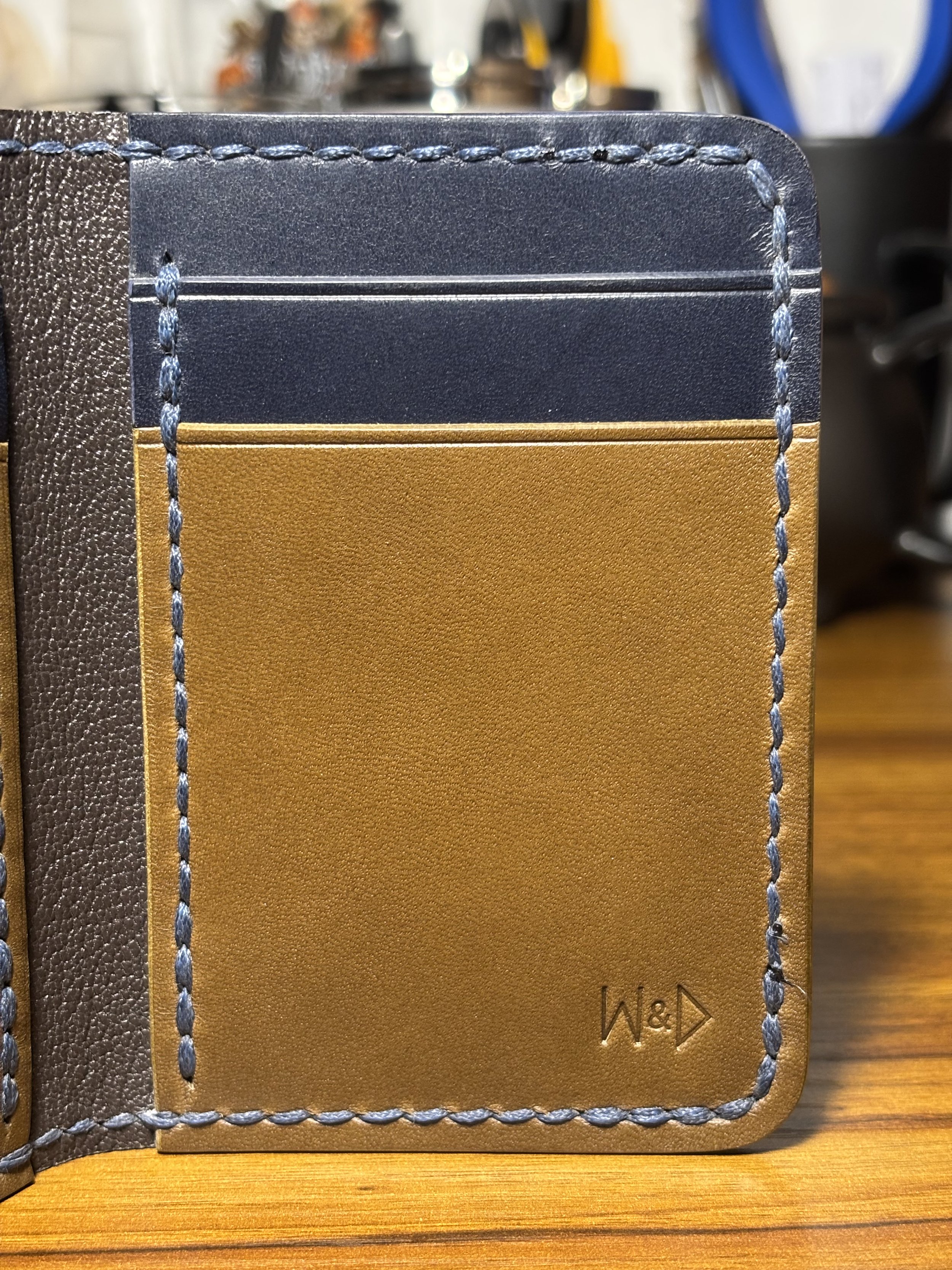 Interior pocket detail of The 1776 Bifold Wallet showing olive green and navy blue leather, hand creasing, saddle stitching, and the debossed maker's mark.