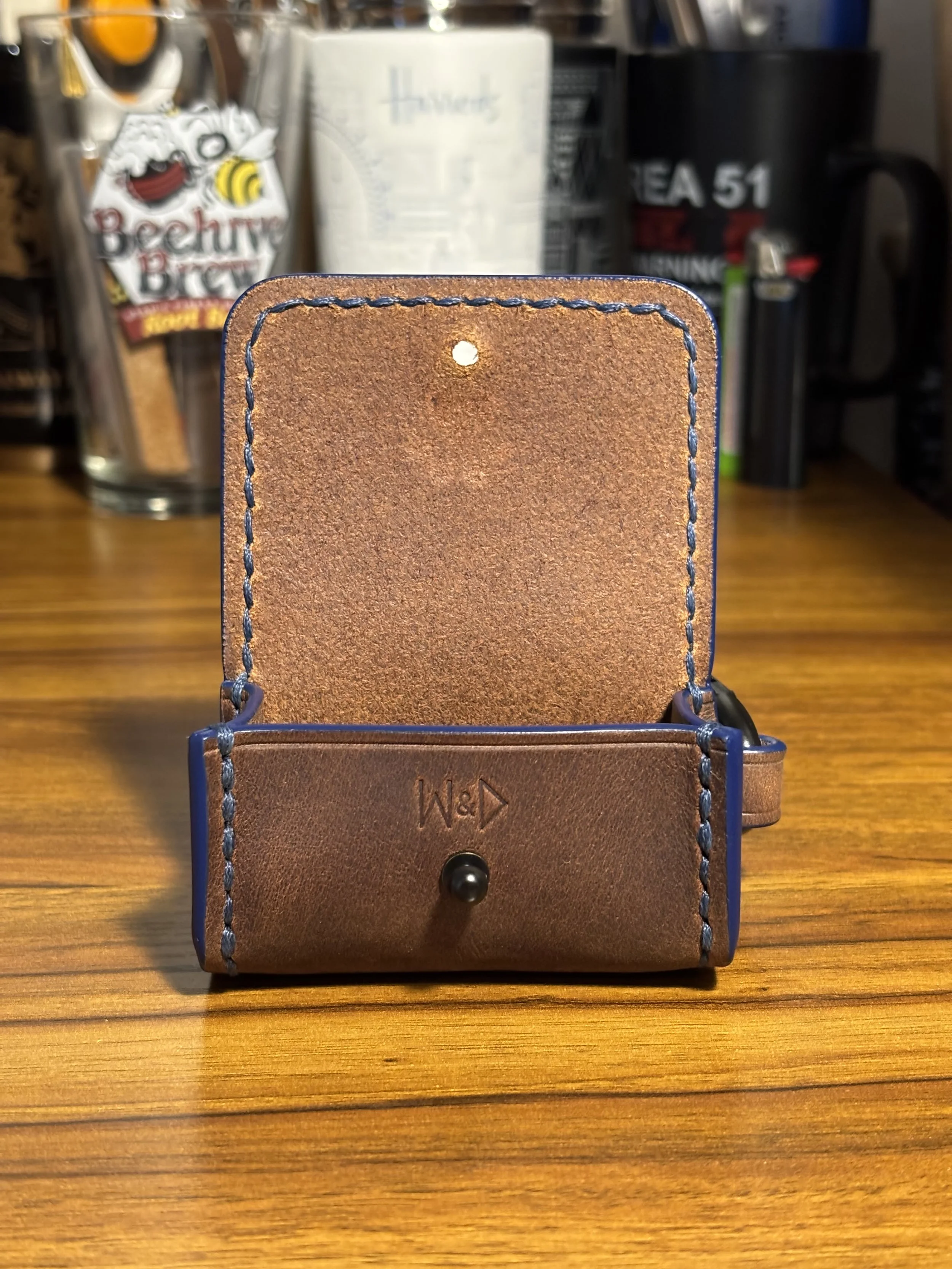 Front view of open leather dog waste bag dispenser showing unlined interior flap, snap button closure, and blue contrast stitching.