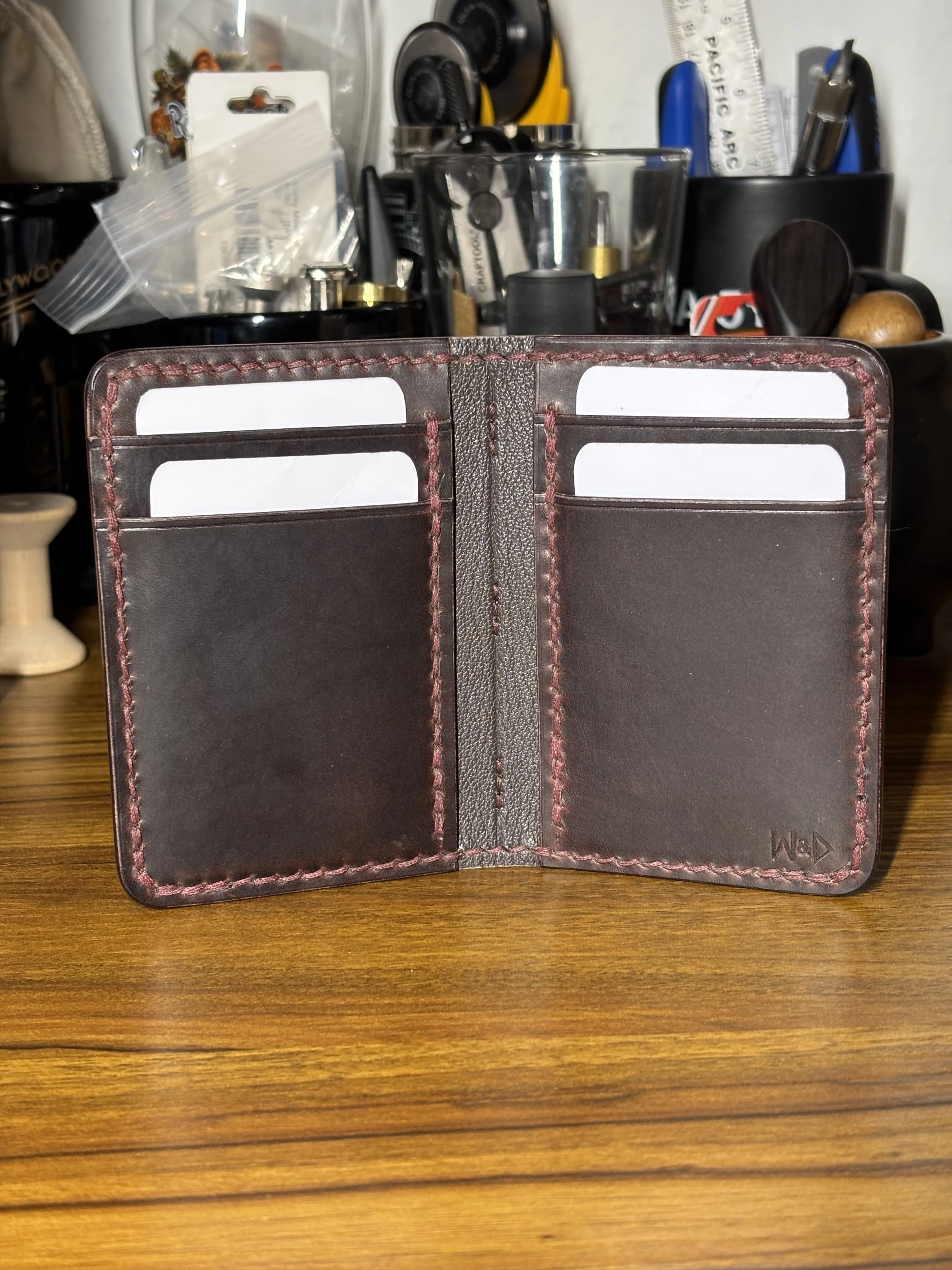 Handcrafted bifold wallet featuring a Horween Dublin shell, Chèvre goat skin lining, hand-skived edges and internals, and Conceria La Bretagna Cowboy pockets on a workshop bench.