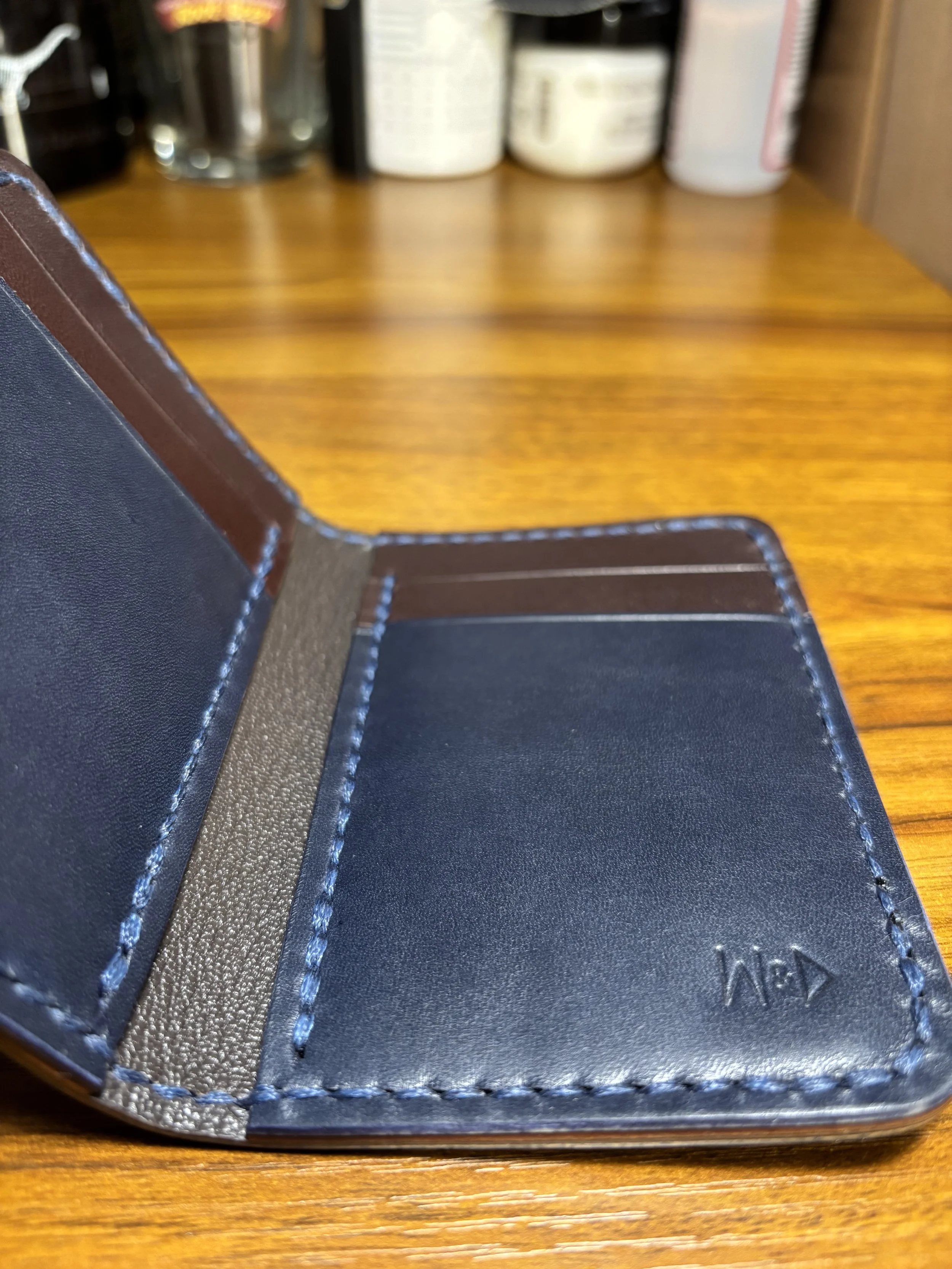 Angled interior view of The Kraken leather bifold wallet showing navy and brown card pockets, saddle stitching, and Chèvre-lined shell.