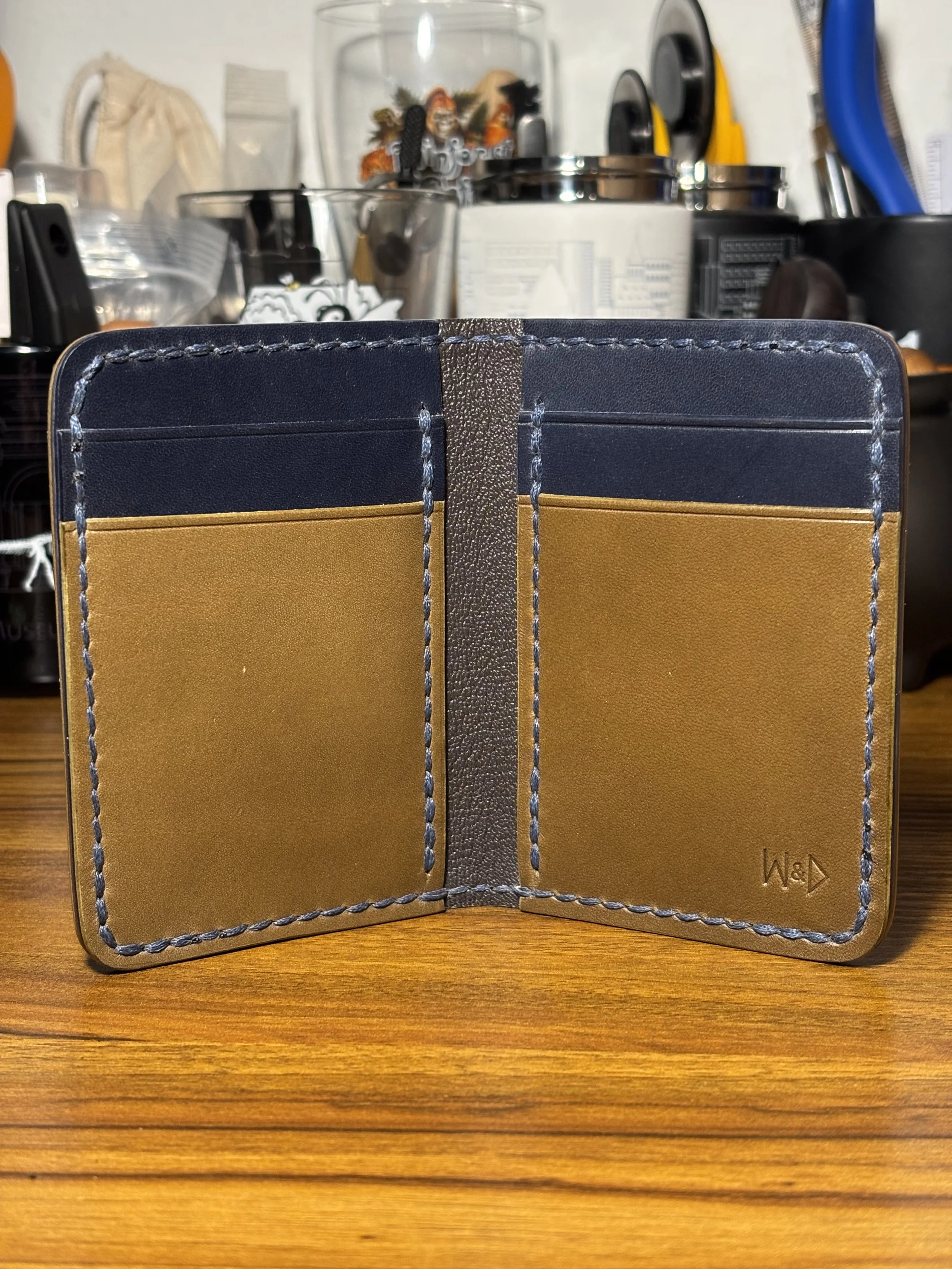 Open view of The 1776 Bifold Wallet showing olive green card pockets, navy blue interior leather, contrasting saddle stitching, and chèvre-lined shell.
