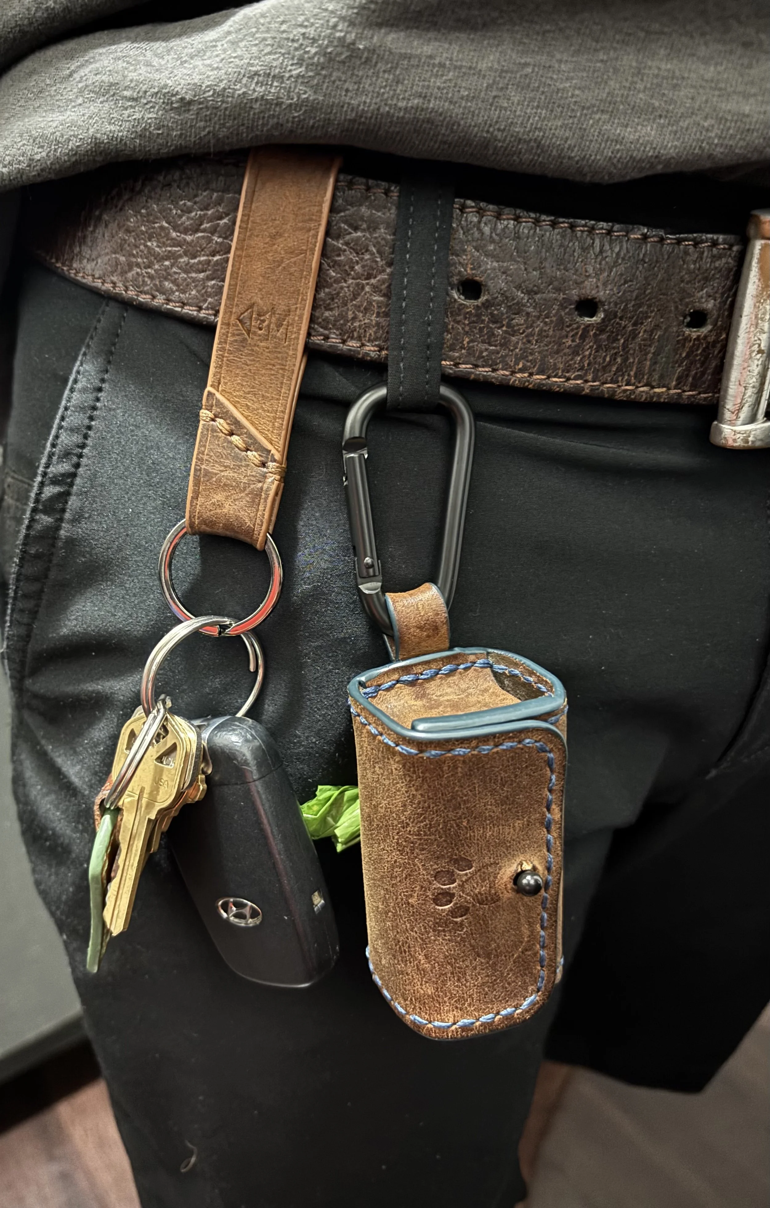 Handcrafted leather dog waste bag dispenser and key fob clipped to a belt loop for everyday carry.