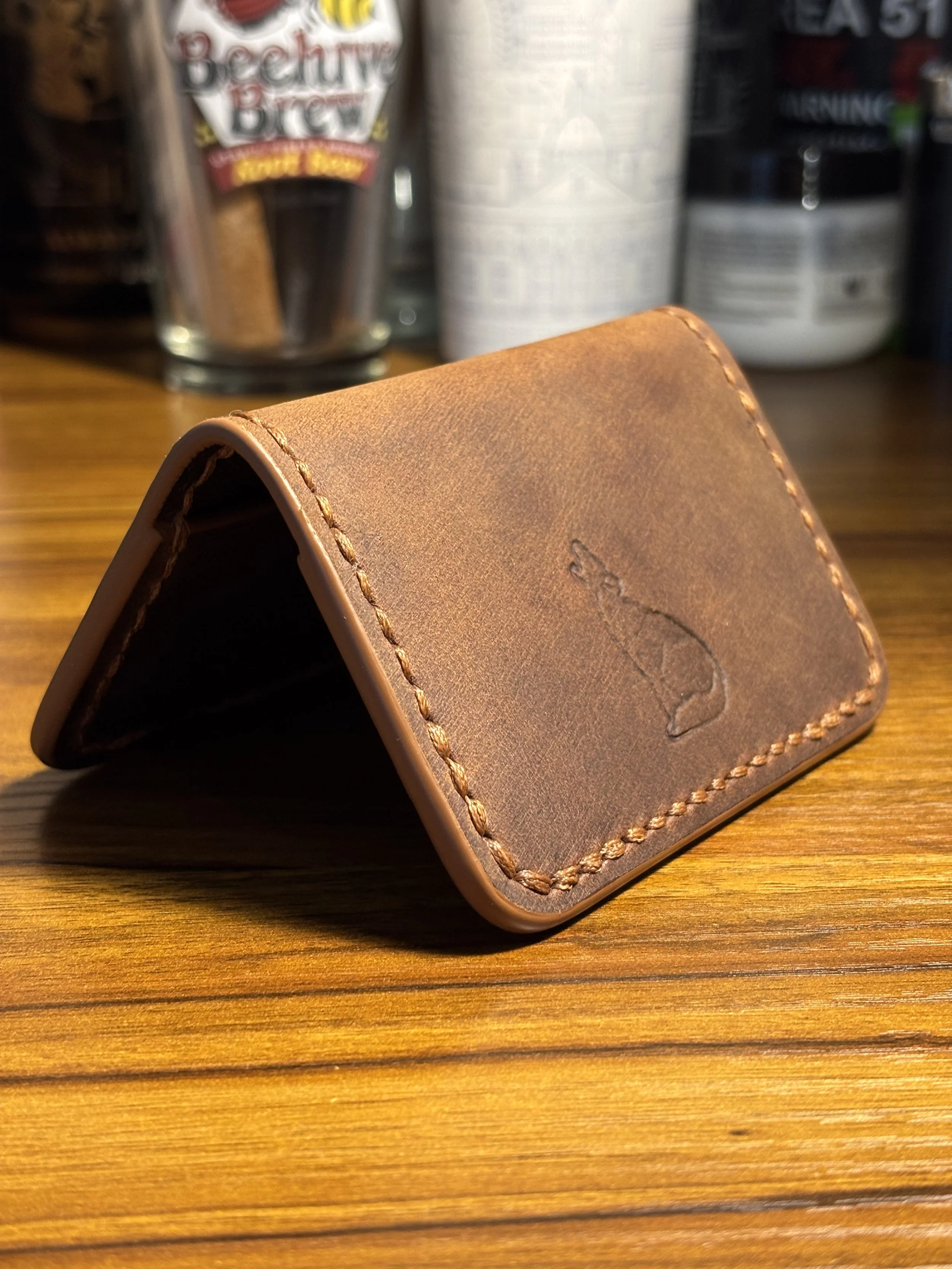 Handcrafted brown leather slim card case standing folded with a stamped howling coyote logo