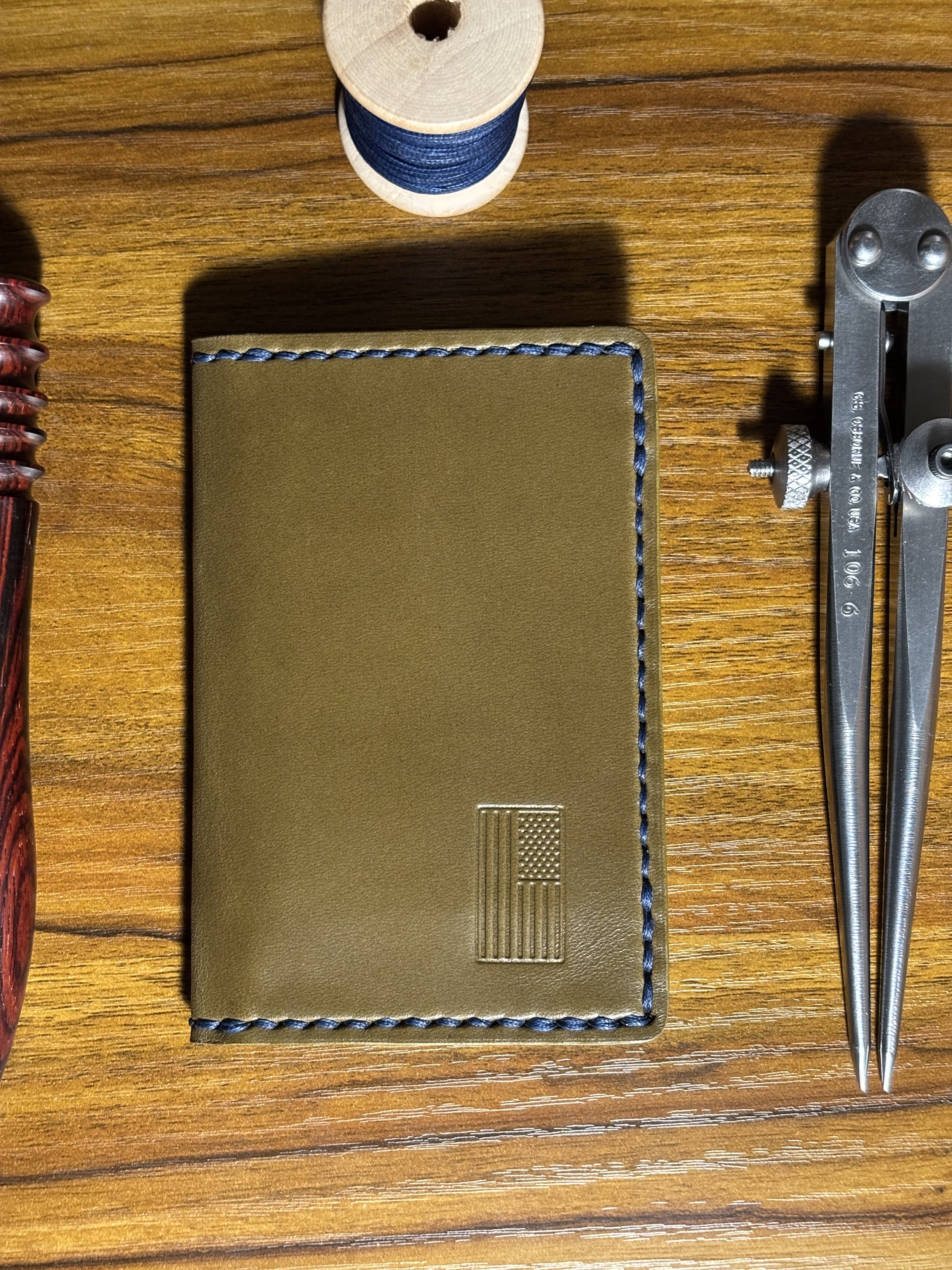 Olive green leather bifold wallet with blue stitching and stamped American flag logo.