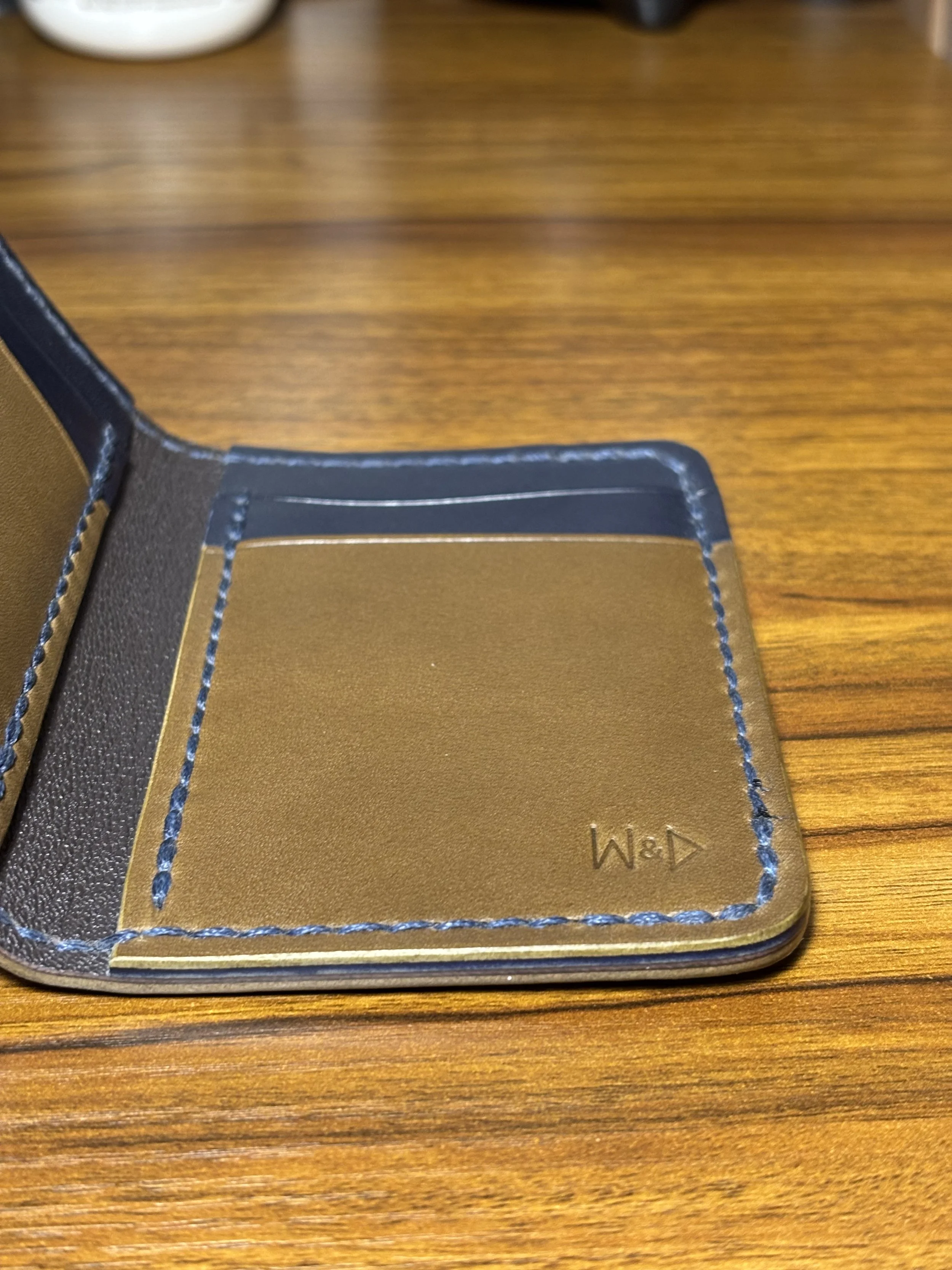 Interior detail of The 1776 Bifold Wallet showing an olive green card pocket, navy blue leather, saddle stitching, and discreet debossed maker's mark.