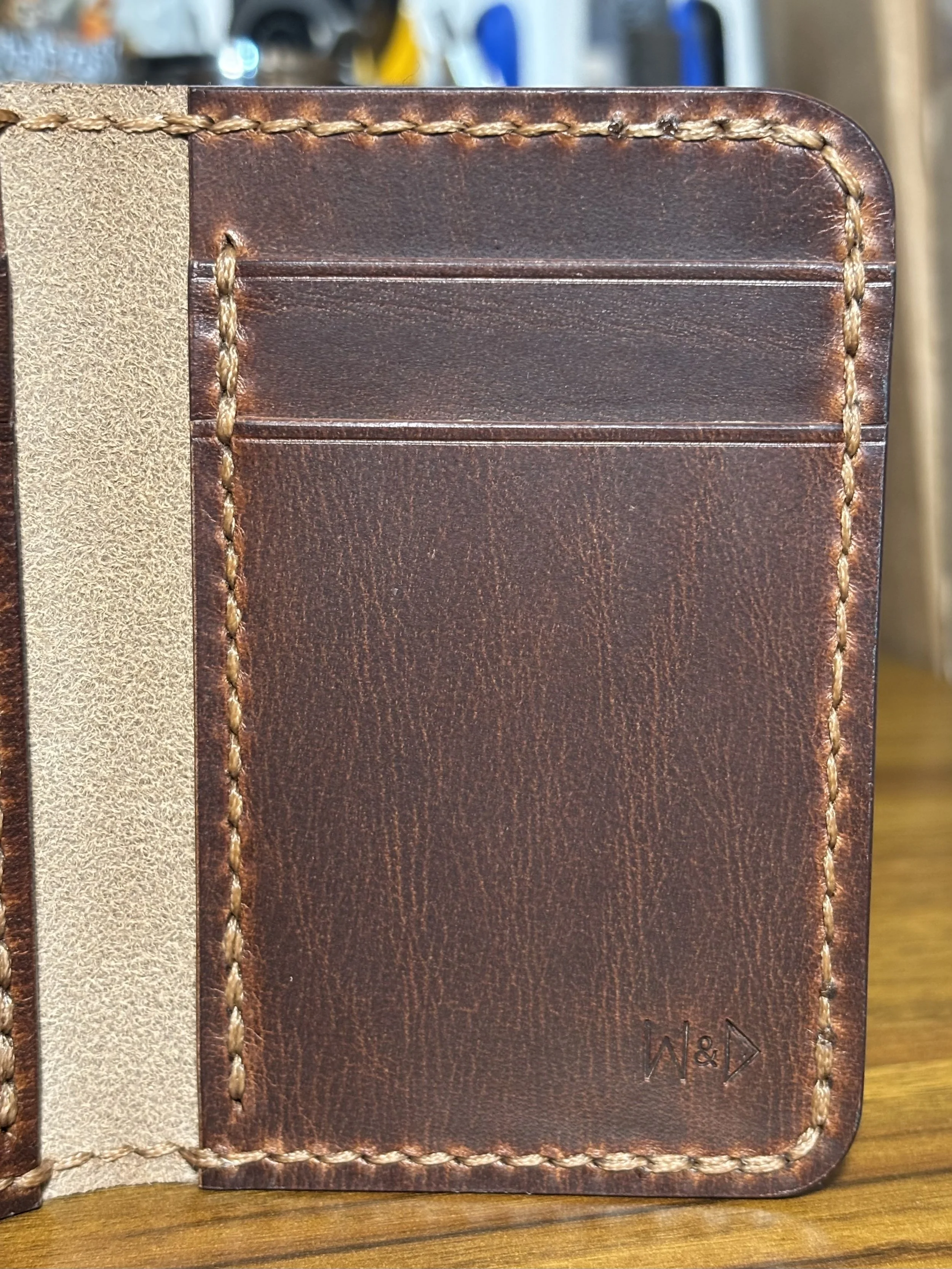 Close-up of interior leather wallet card slots showing hand saddle stitching, creased edges, and maker's mark stamp.