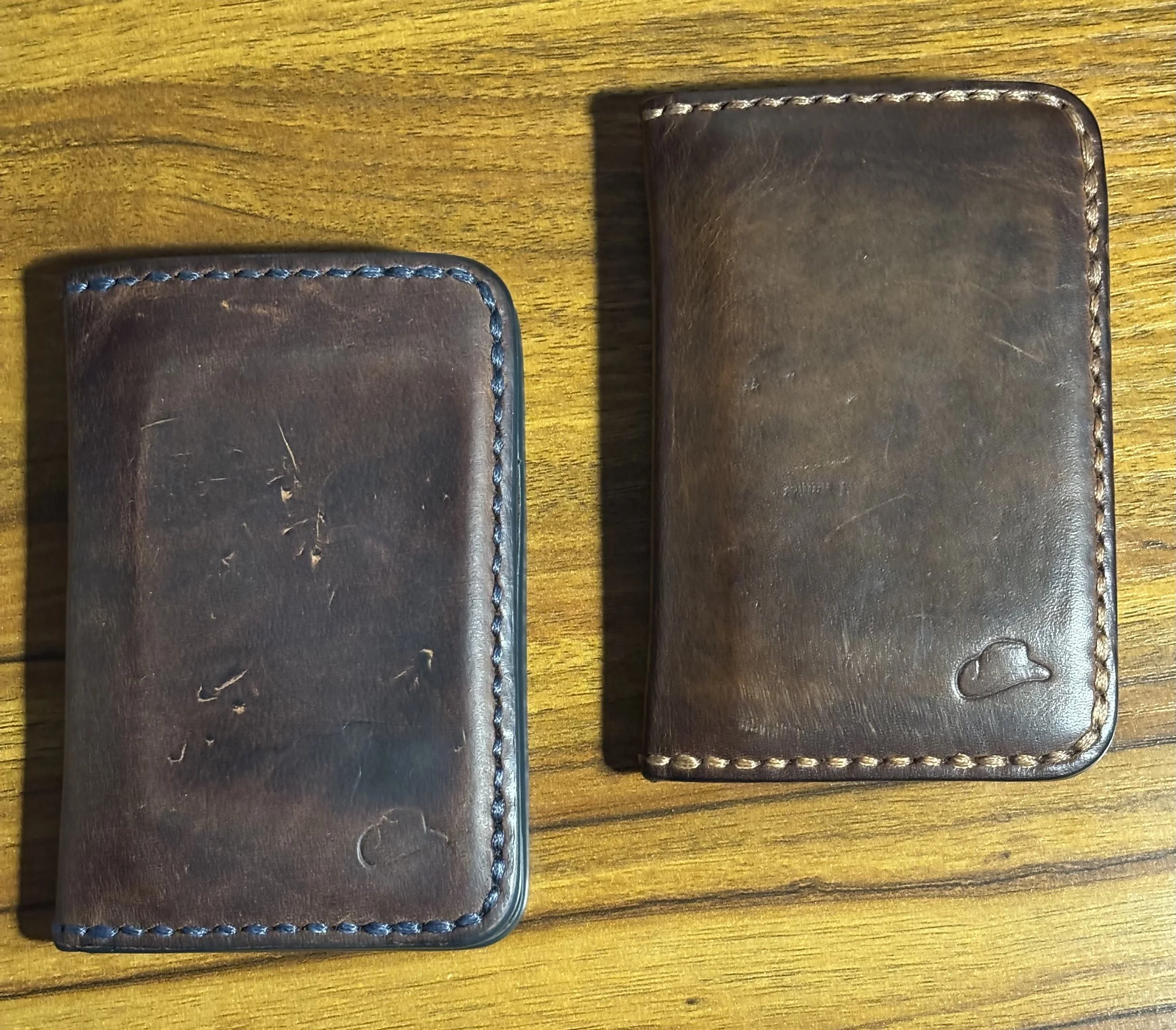Pair of well-worn handcrafted brown leather bifold wallets showing rich patina and saddle stitching on a wooden surface.