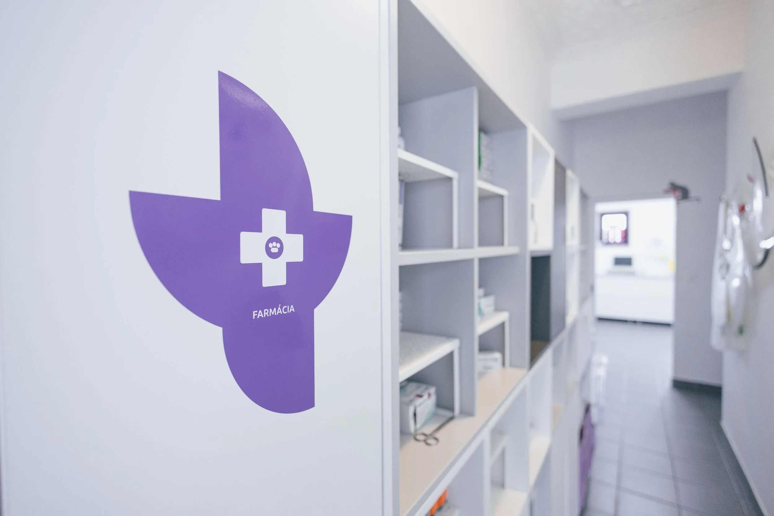 Sinal de farmácia em uma parede branca com estantes ao fundo em um ambiente de clínica ou hospital.