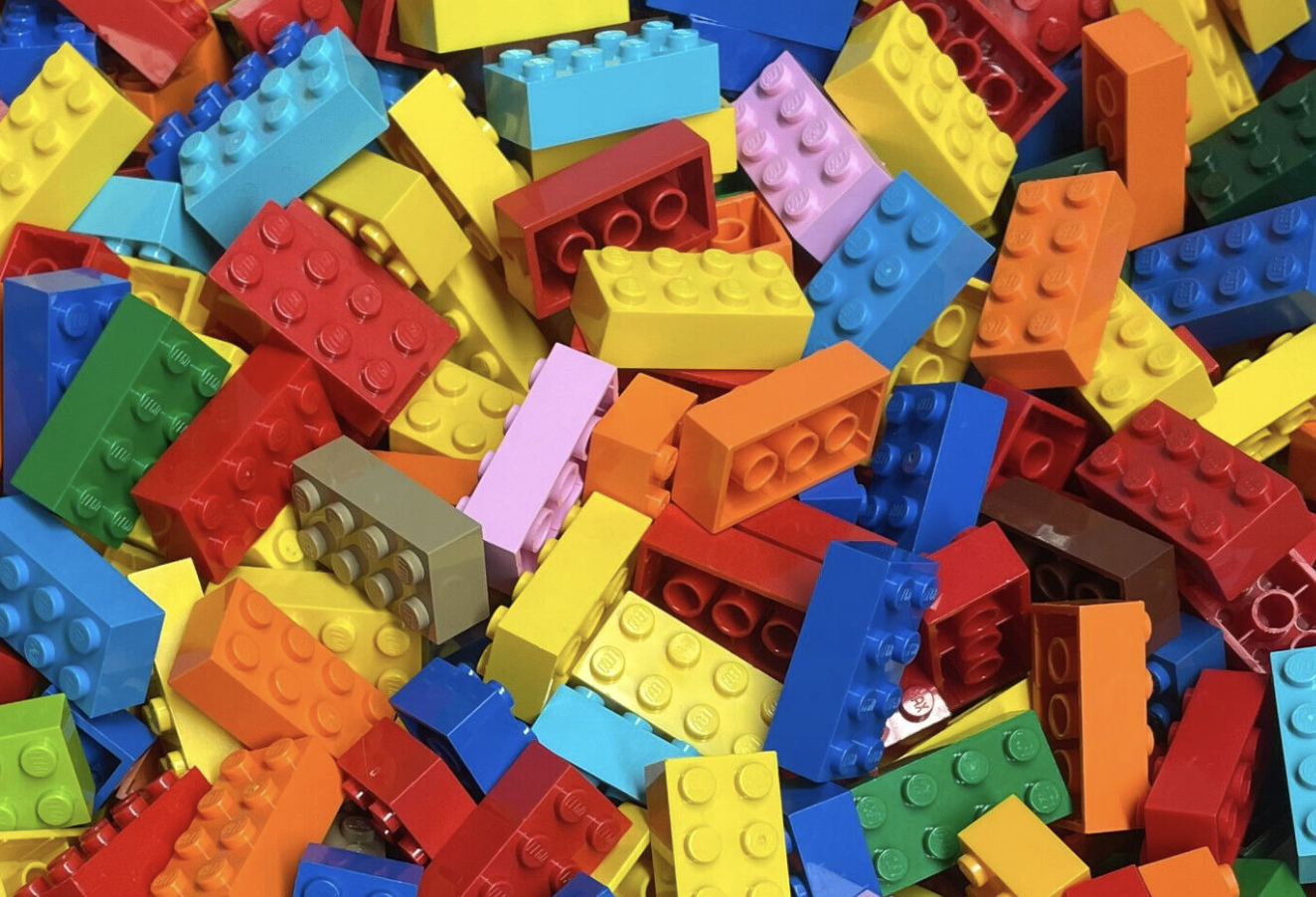 A colorful pile of LEGO bricks in red, yellow, blue, green, orange, pink, gray, and brown.