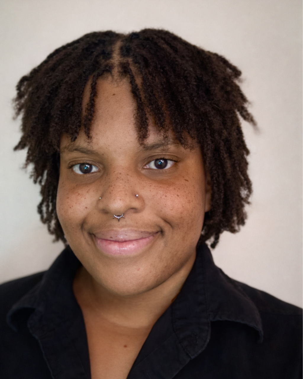 Portrait of a woman with shoulder-length curly hair wearing a gray sweater, smiling against a plain background.