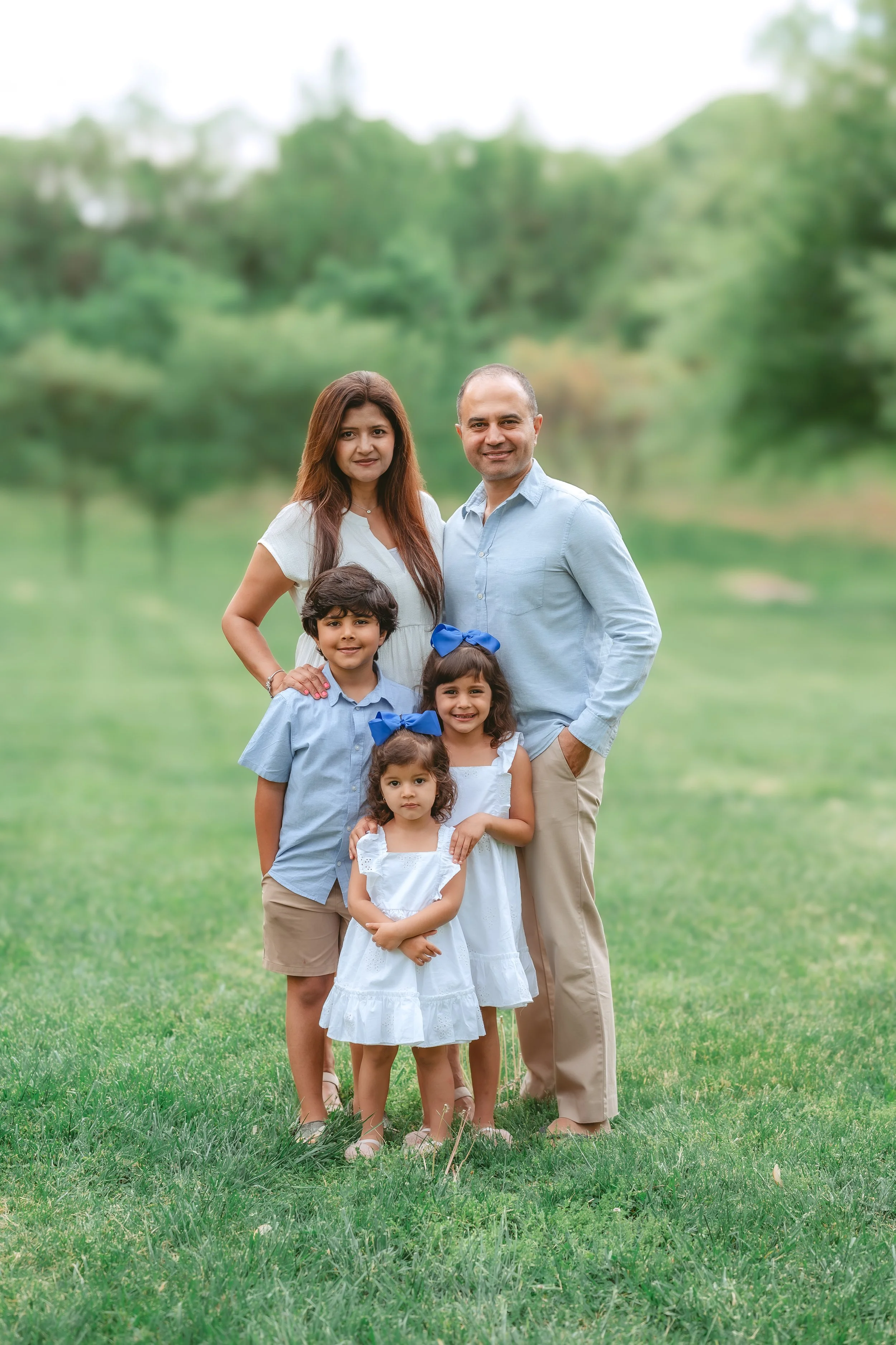 Family of five posing during a light and airy outdoor portrait session in Gaithersburg, Maryland, wearing coordinated blue and white outfits.