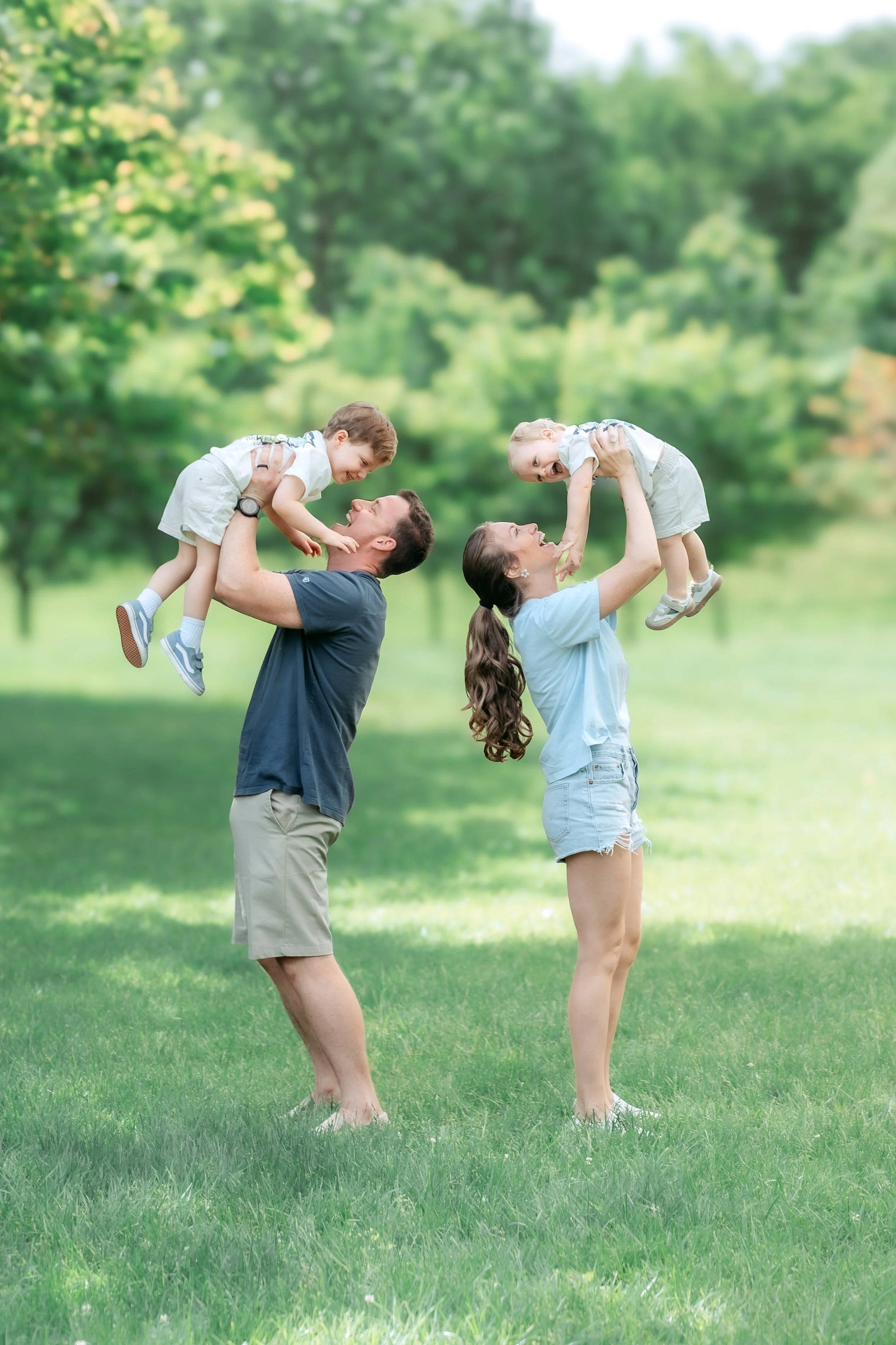 Parents lifting toddlers during a joyful, light and airy family session in a grassy park near Gaithersburg, Maryland.