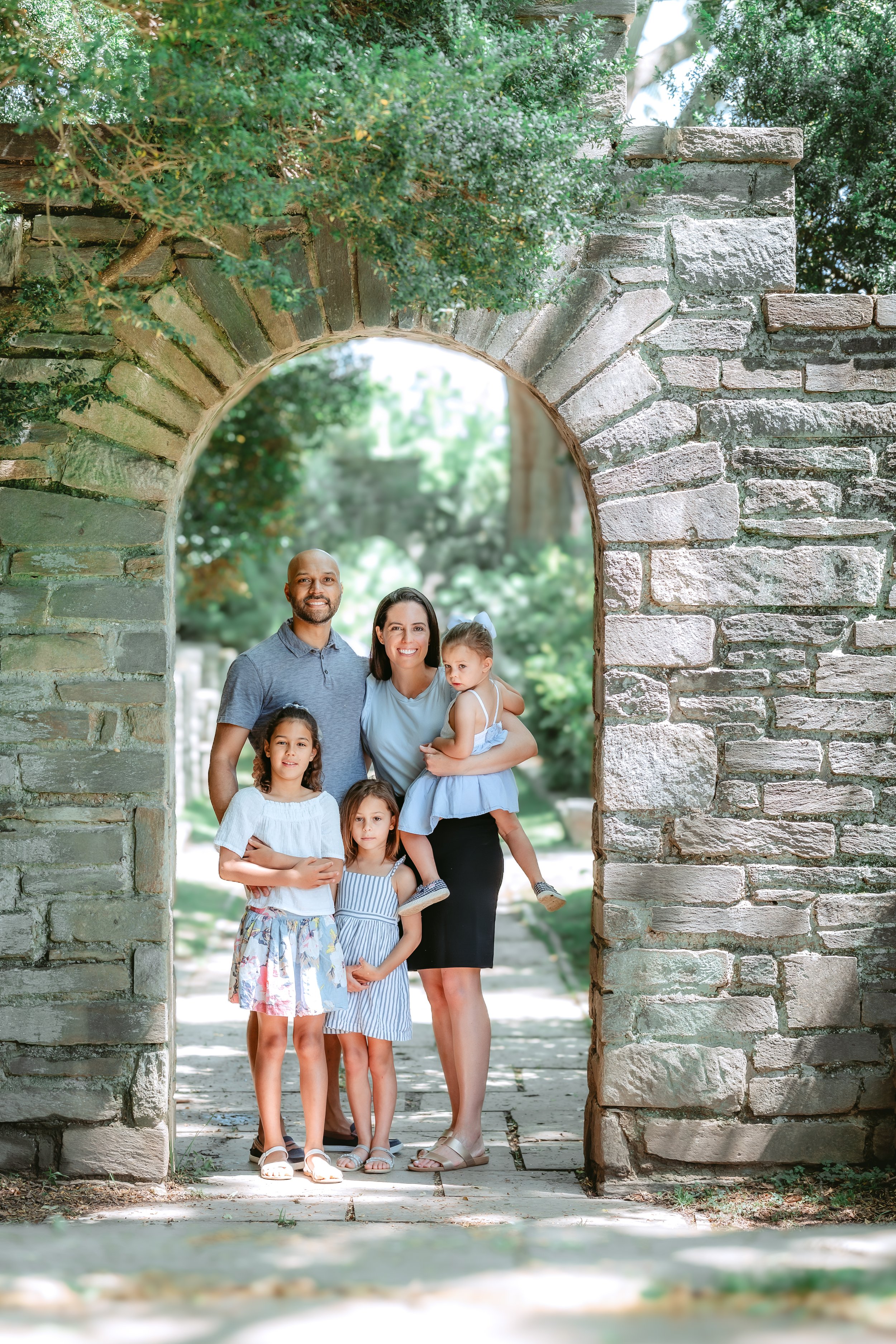 Family of five under stone arch during light and airy summer photo session in Rockville, MD.