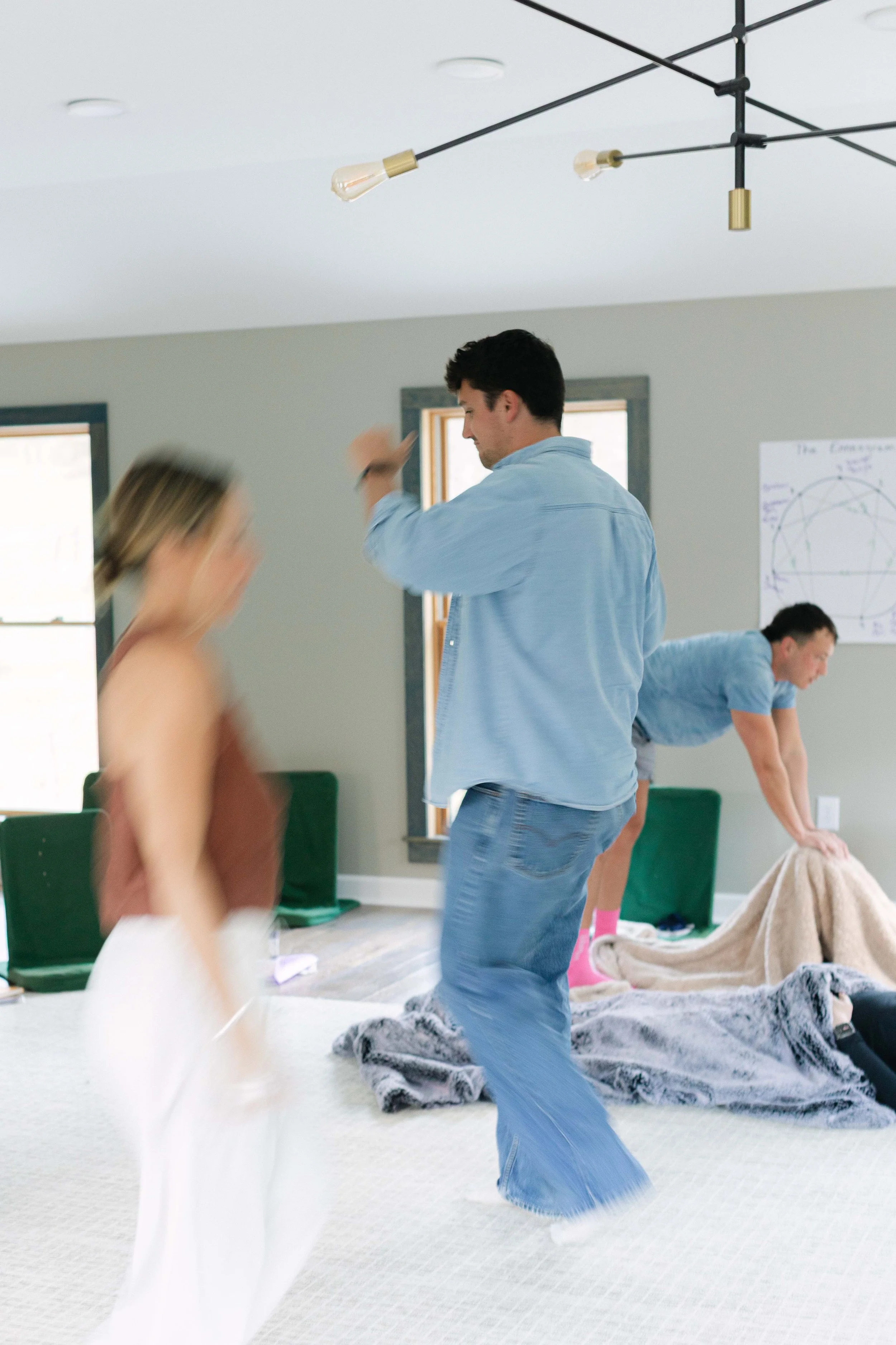 People dancing and moving around in a room with large windows and a chalkboard with a diagram on it.