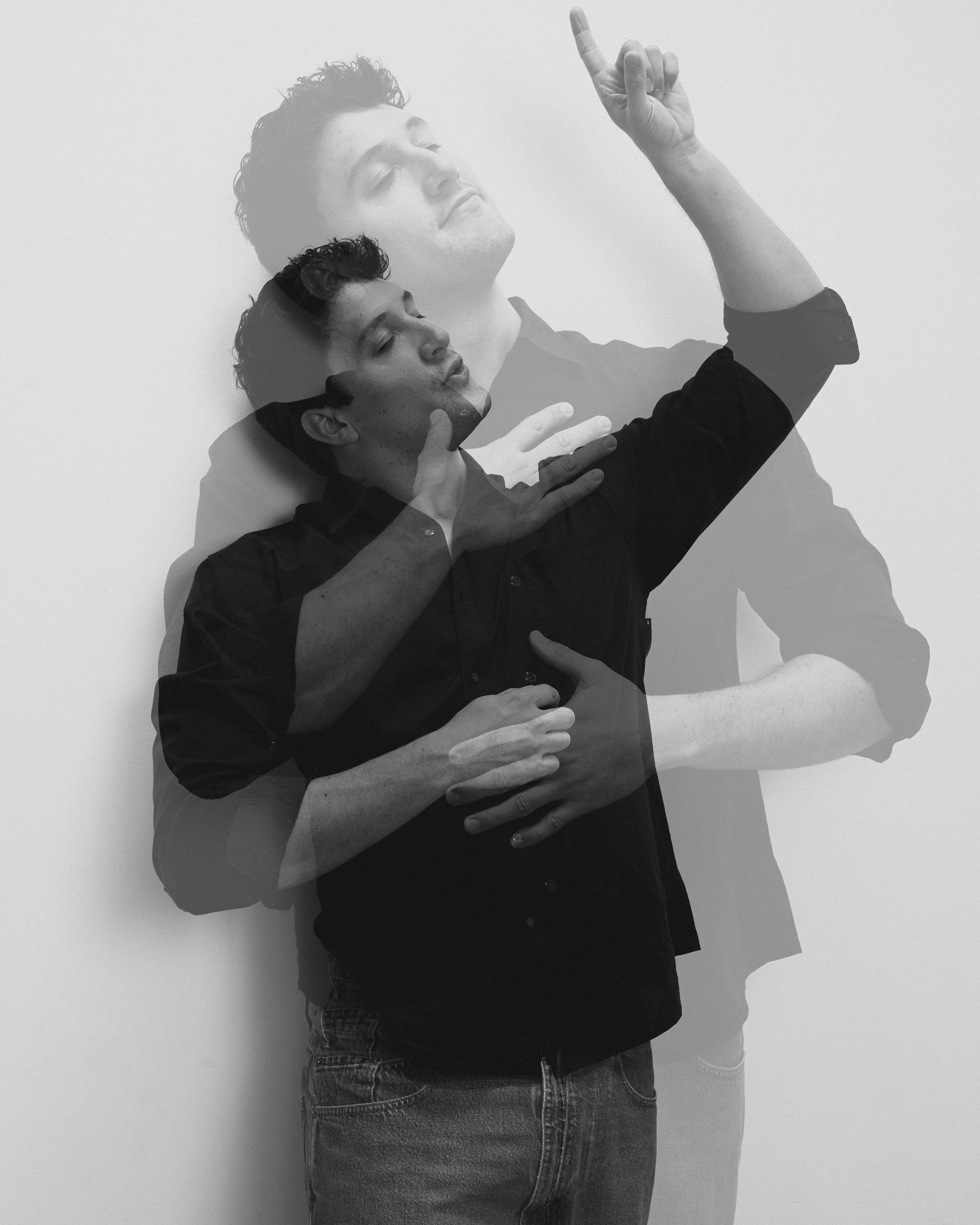 A black and white photo of a young man with curly hair, multiple exposures creating a layered effect. He is gently holding his neck with one hand and pointing upwards with the other while looking relaxed.