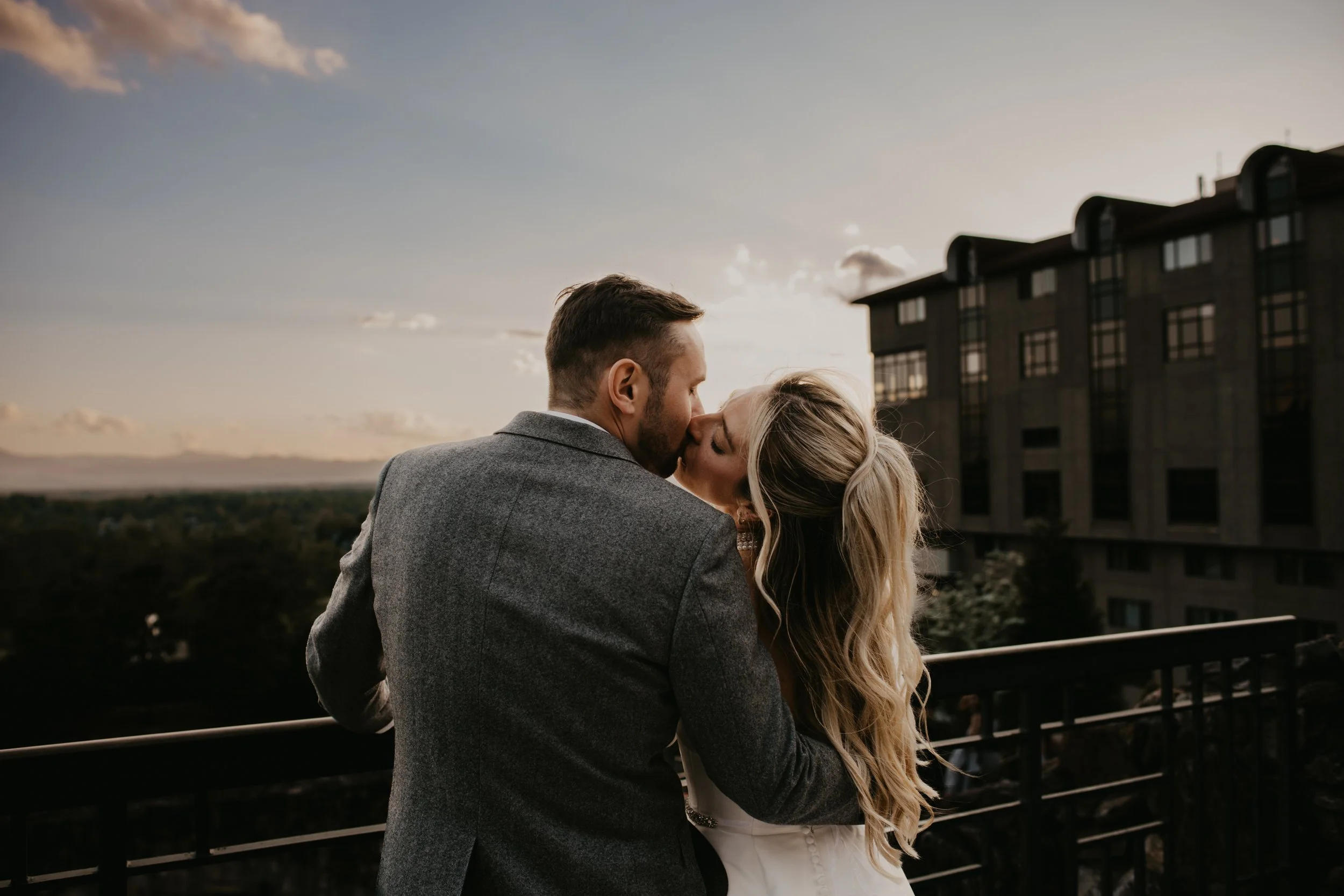 bride and groom kissing in front of a sunset sky 