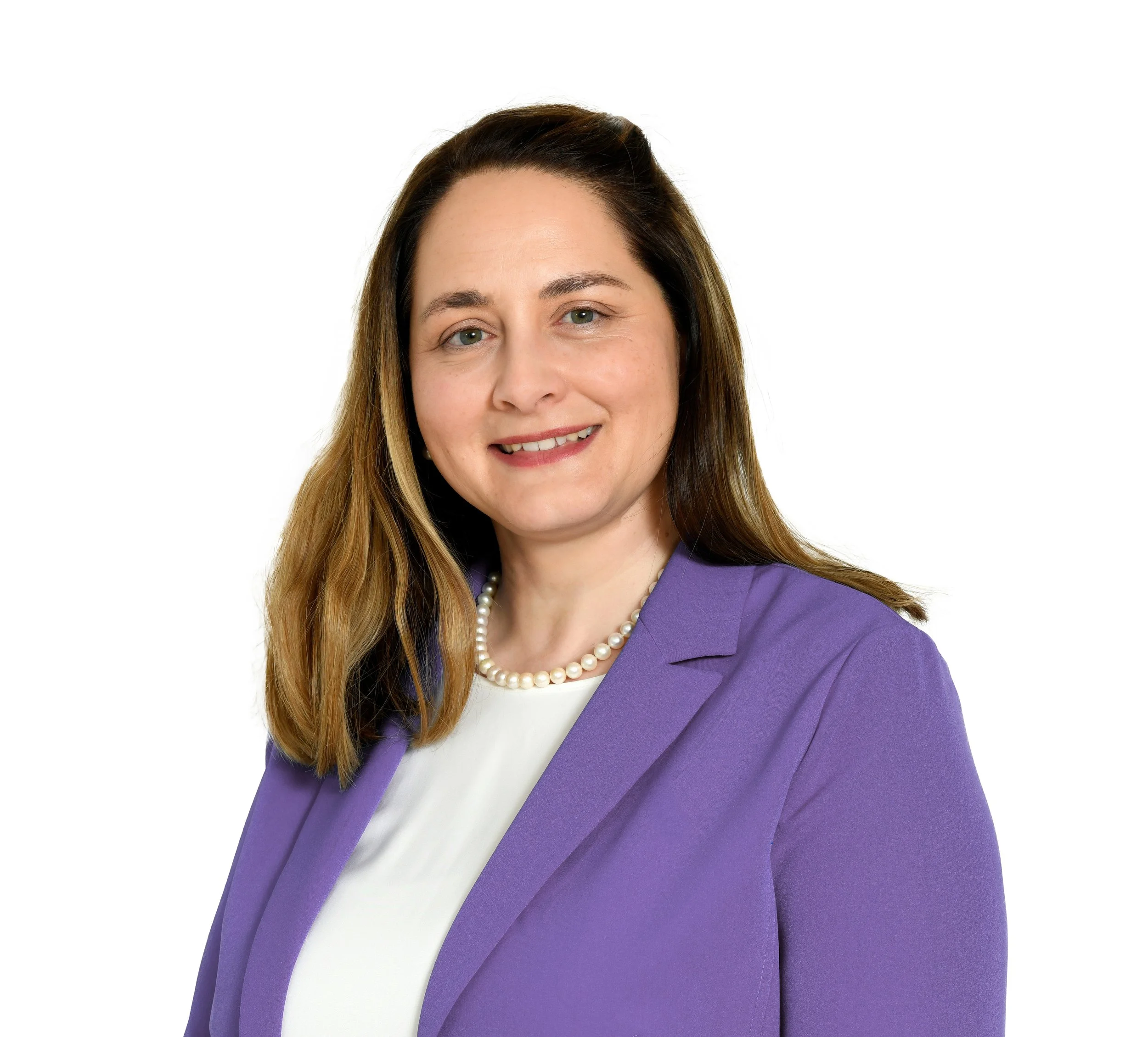 Dame mit braunen, leicht gewellten Haaren, trägt eine lila Blazer und eine Perlenkette, vor weißem Hintergrund.
